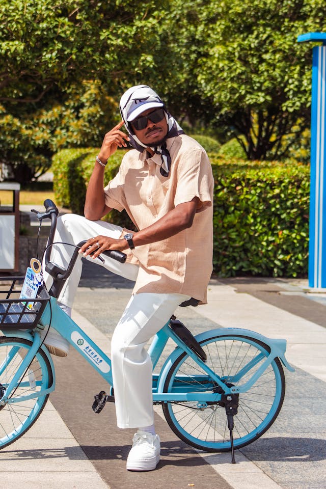 A stylish man wearing a headscarf and sunglasses poses on a light blue bicycle