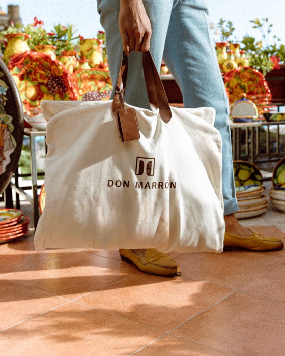 A Don Marrón garment bag rests beside a table in Italy, symbolizing artisanal craftsmanship and timeless design.