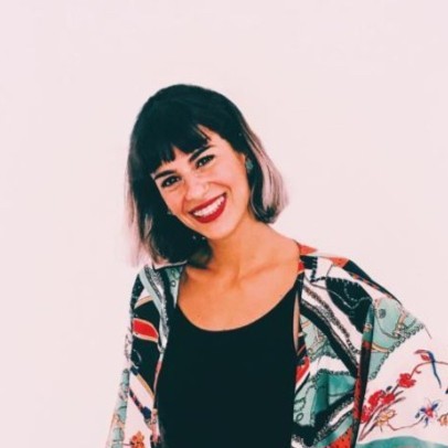 Donna sorridente con capelli scuri e frangia, che indossa un top nero e una giacca colorata