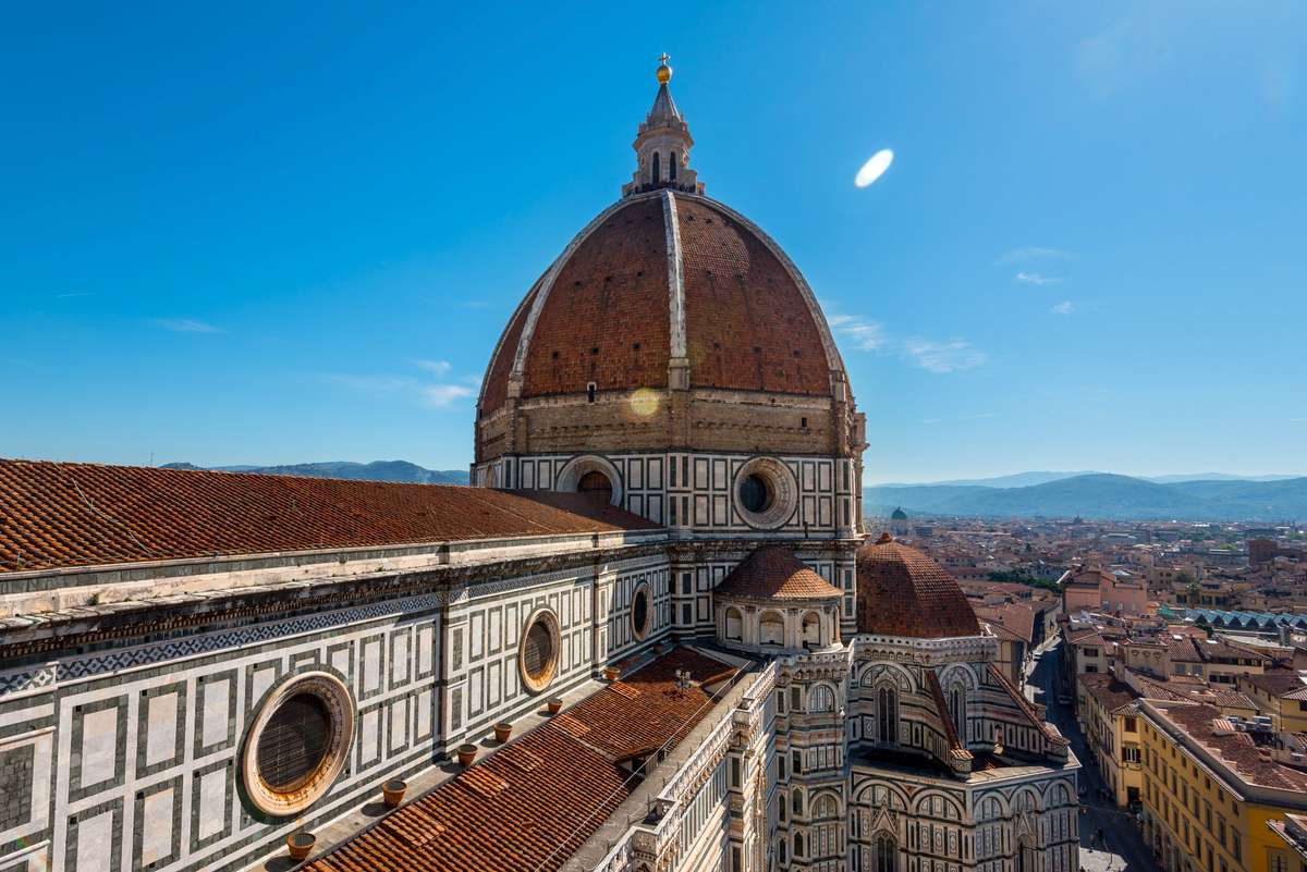 A high-angle view of the dome and tiled facade of a Renaissance cathedral under a clear blue sky in Florence.