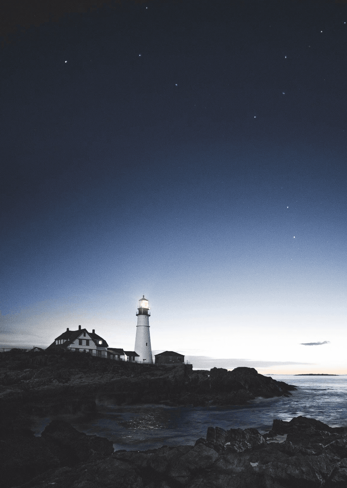 lighthouse beside house near the edge of stone island during day