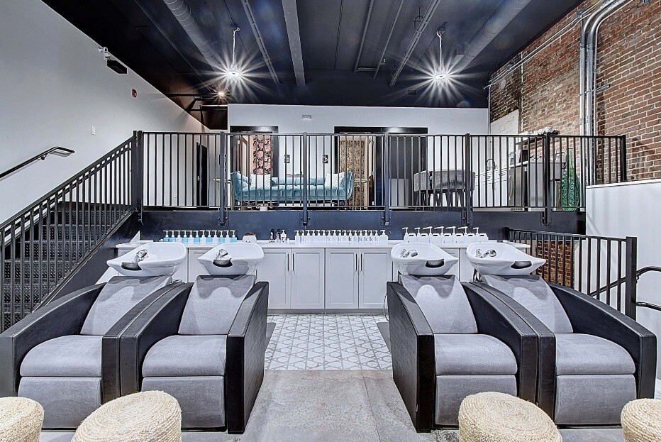 A modern hair wash area featuring cozy seating, wood accents, and industrial decor under soft lighting.