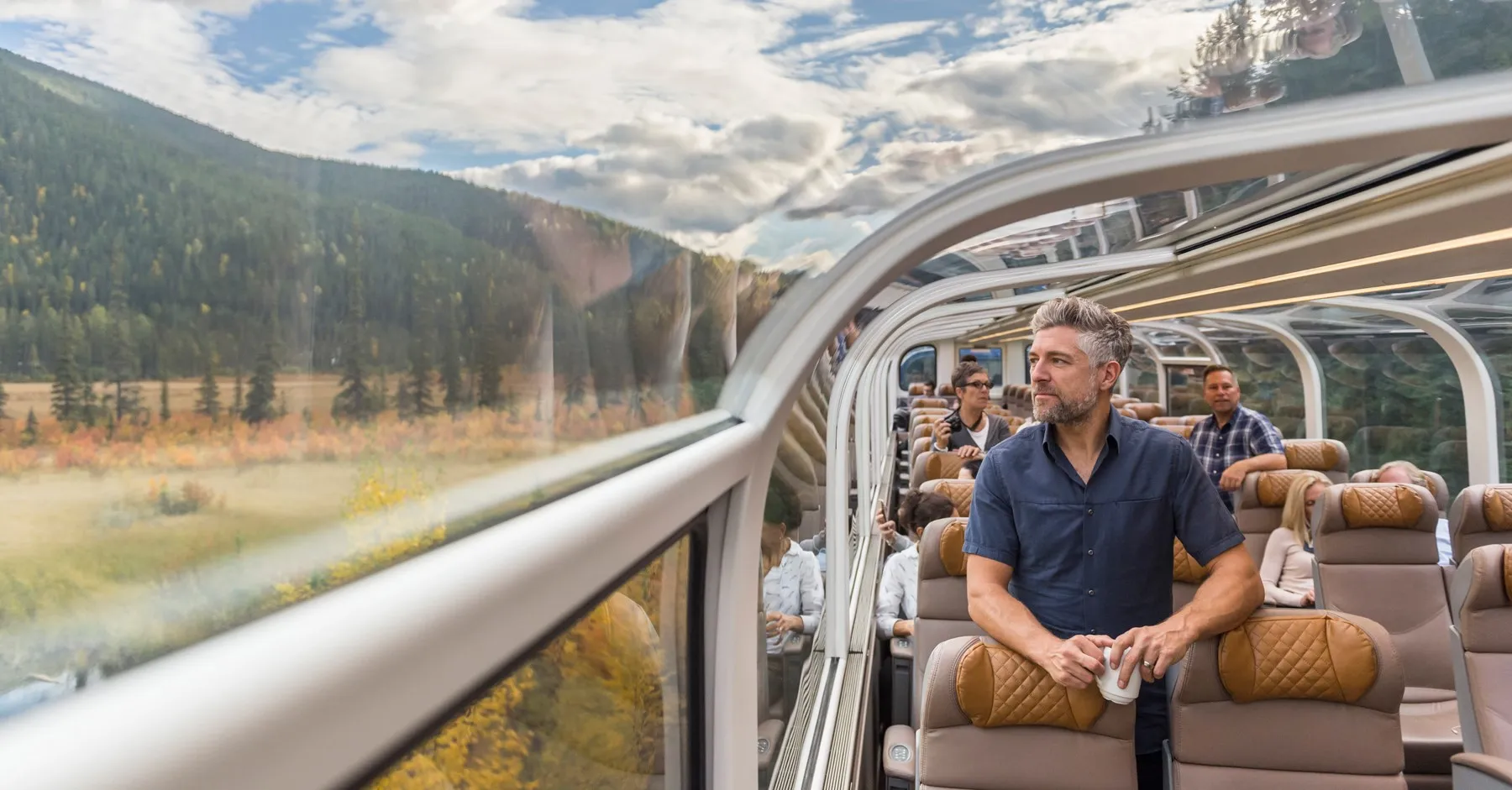 Passengers riding a glass-roof scenic train through a mountain landscape