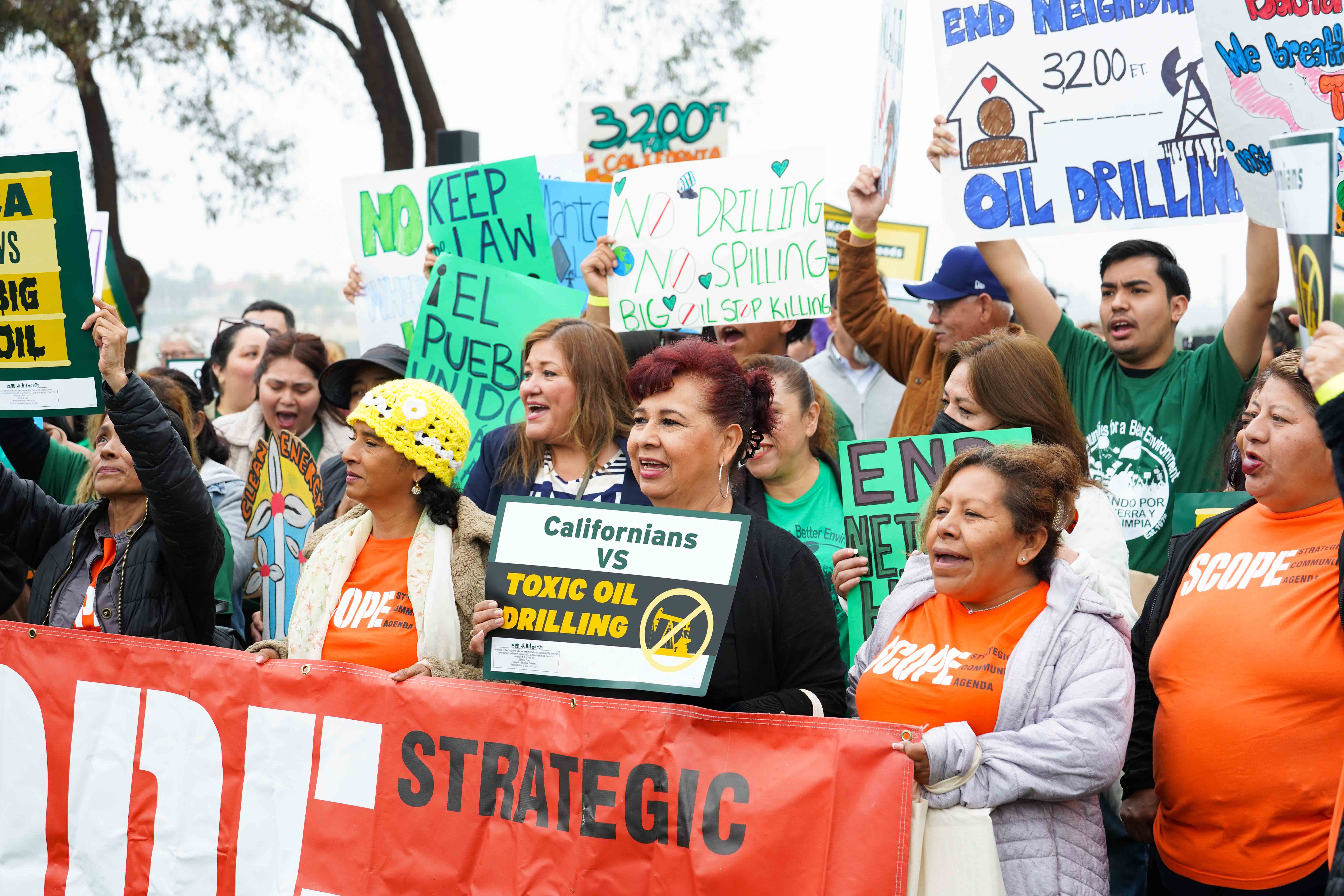 A large crowd of activists against Big Oil with the main focus being a woman holding a sign that says "Californians vs. Toxic Oil drilling"