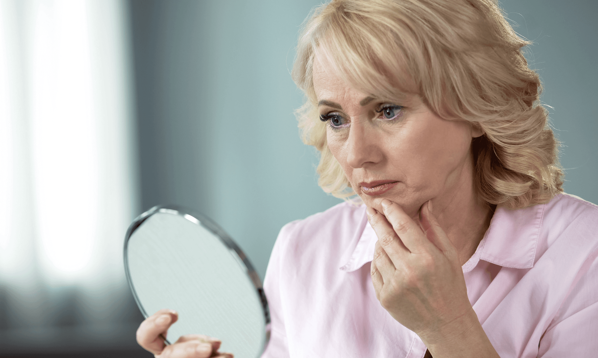 woman looking at aging skin in mirror