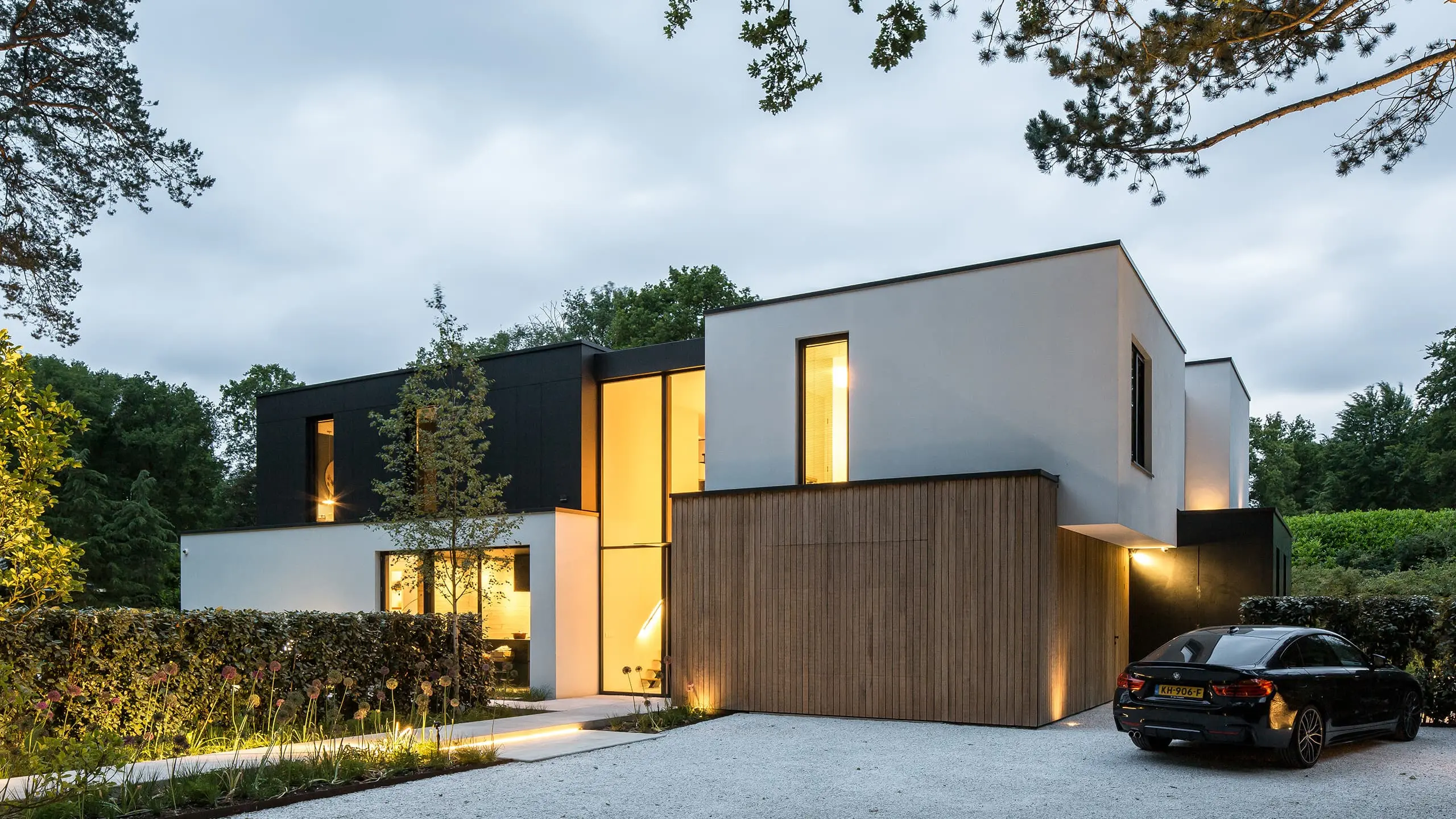 Moderne vrijstaande villa met houten gevelbekleding, grote ramen en verlichte entree tussen het groen