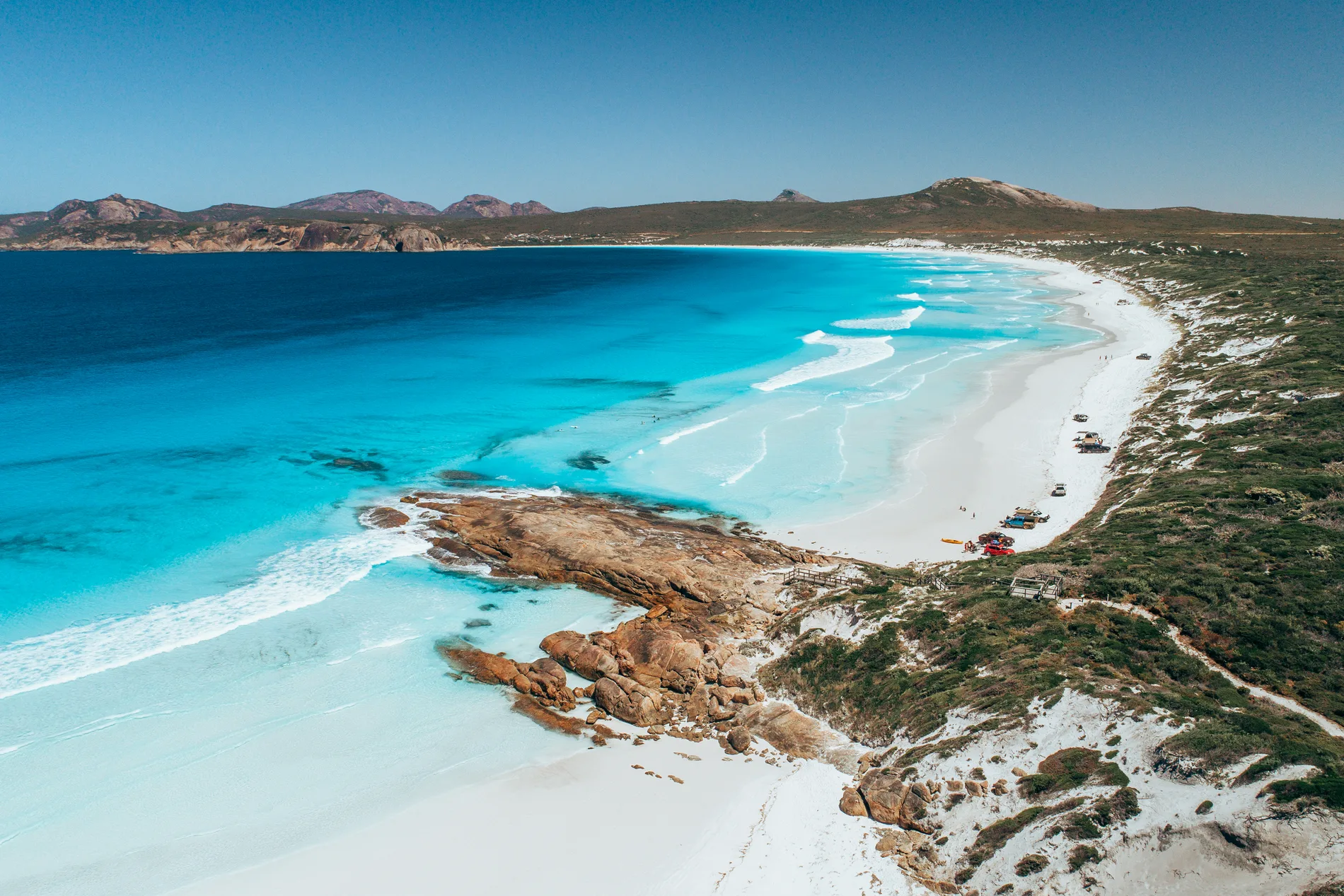 Aerial of a broad bay with white sand, turquoise water and hills beyond