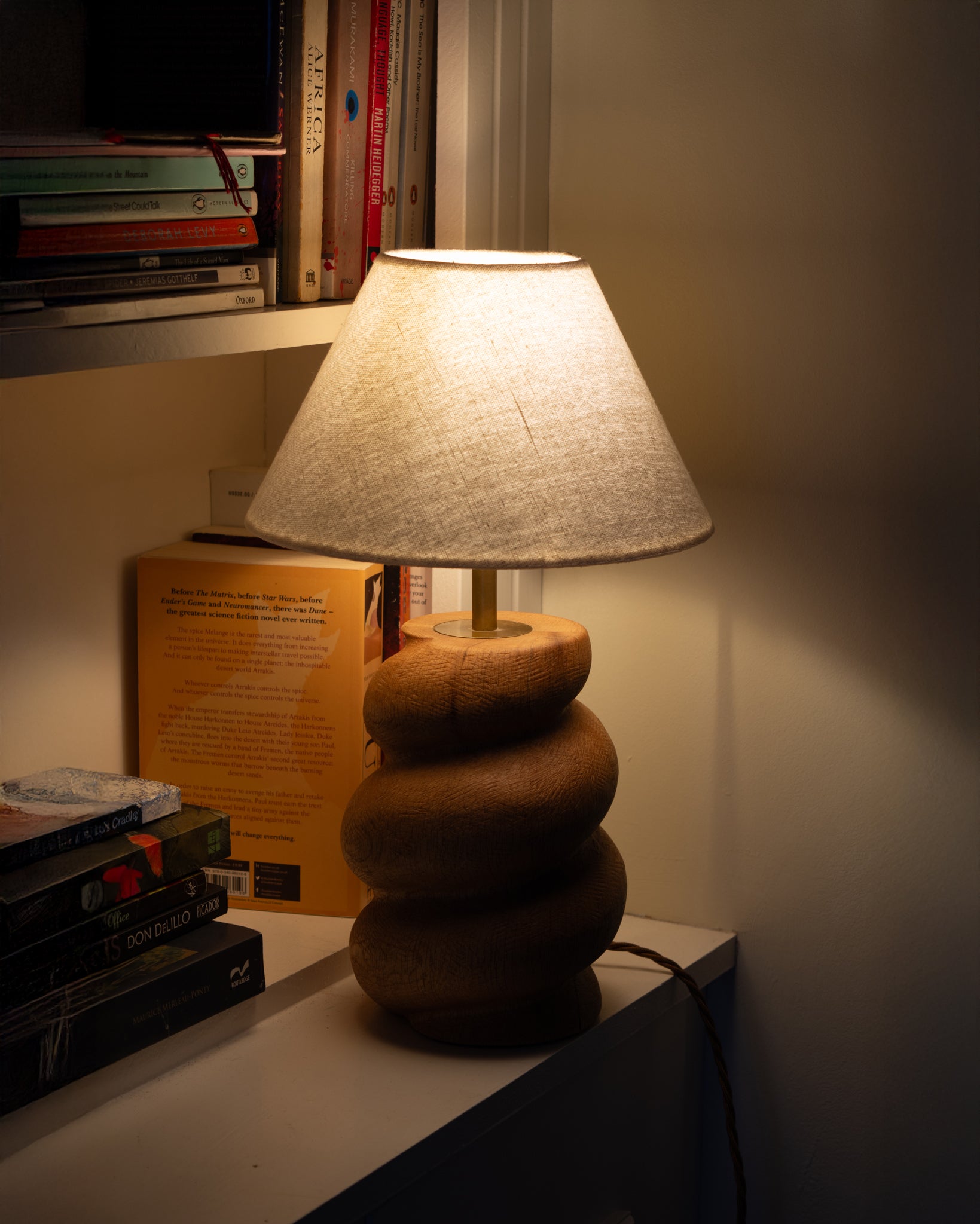 Caracol Table Lamp in Oak lit against bookcase