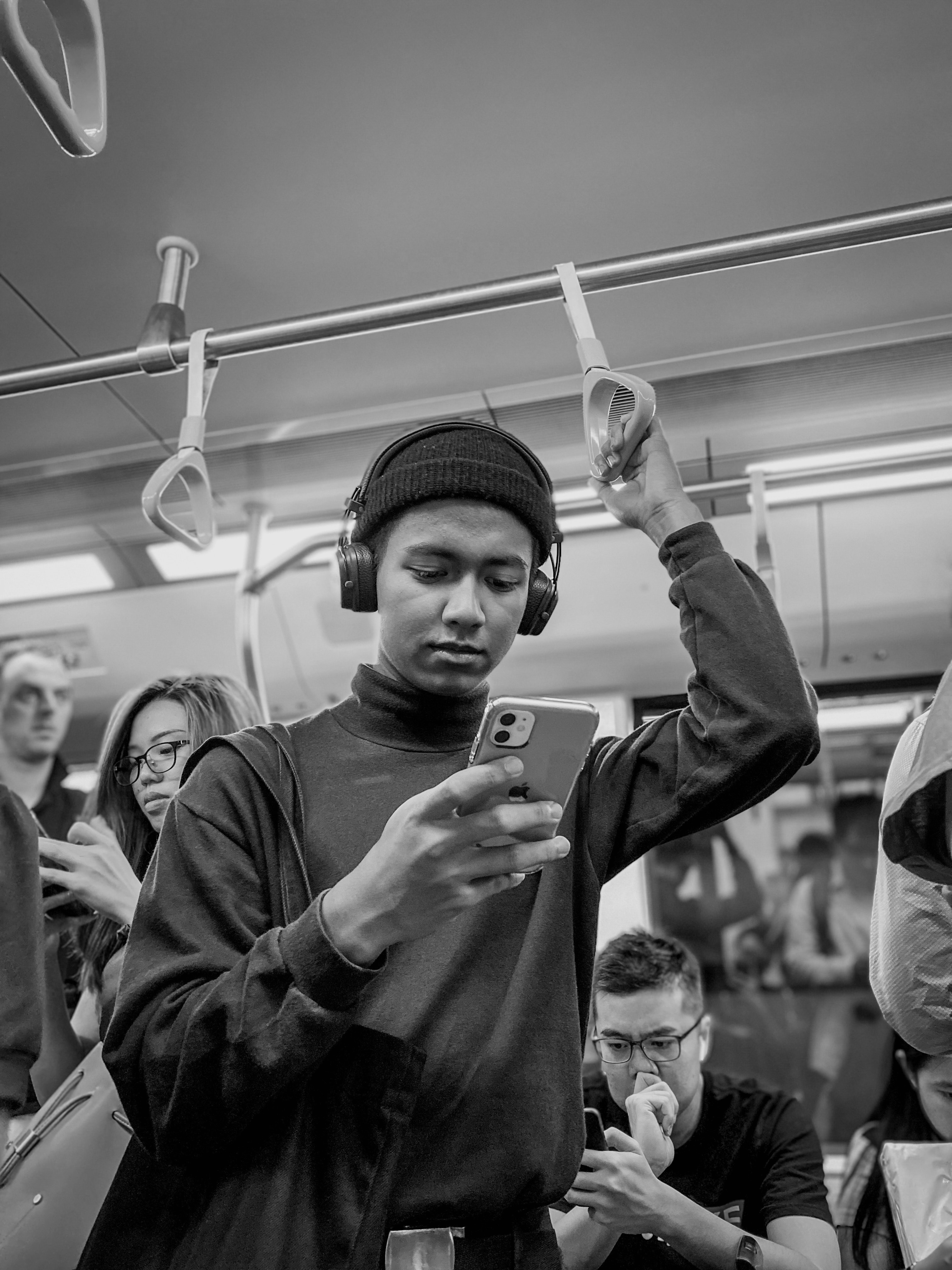 A person in a black outfit holds up a finger in a crowded subway car, engaged with their phone.