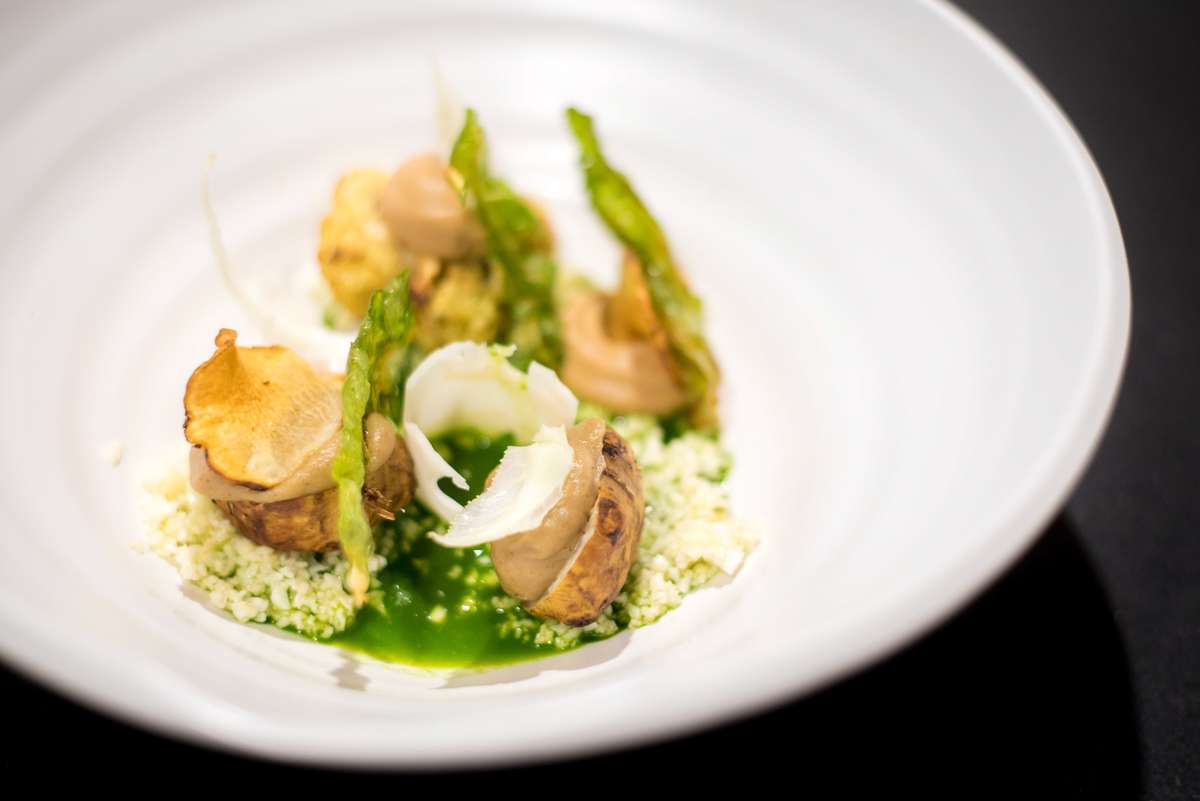 A gourmet dish featuring roasted potatoes and green beans served over a bed of grains and green sauce in a white bowl.
