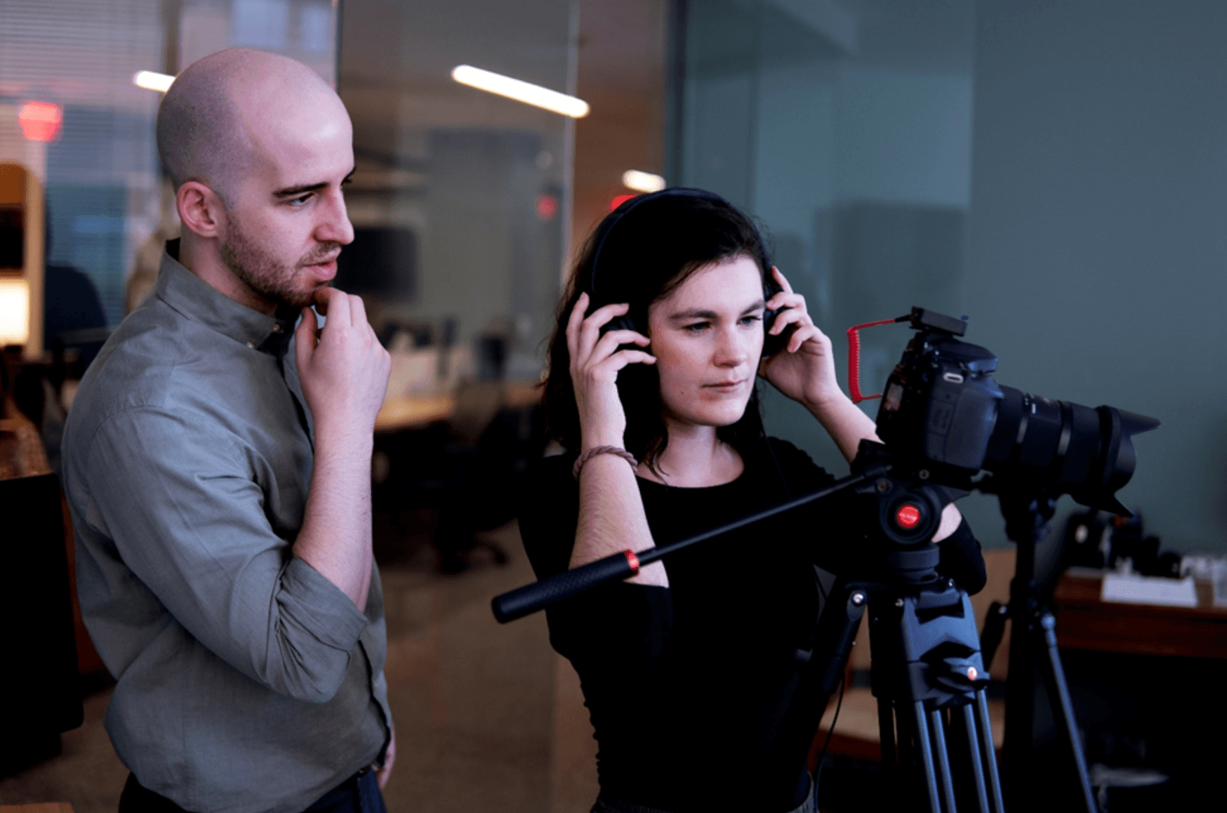 Two individuals collaborating in a production setup—one adjusting headphones, the other directing—illustrating multimedia or podcast creation.
