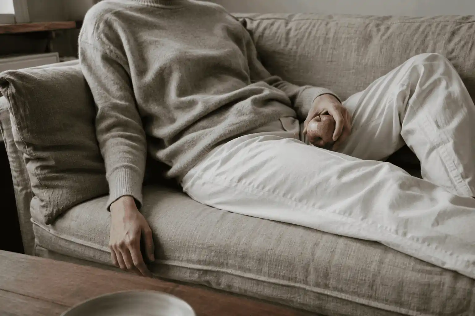 A person resting on a sofa while loosely holding an apple