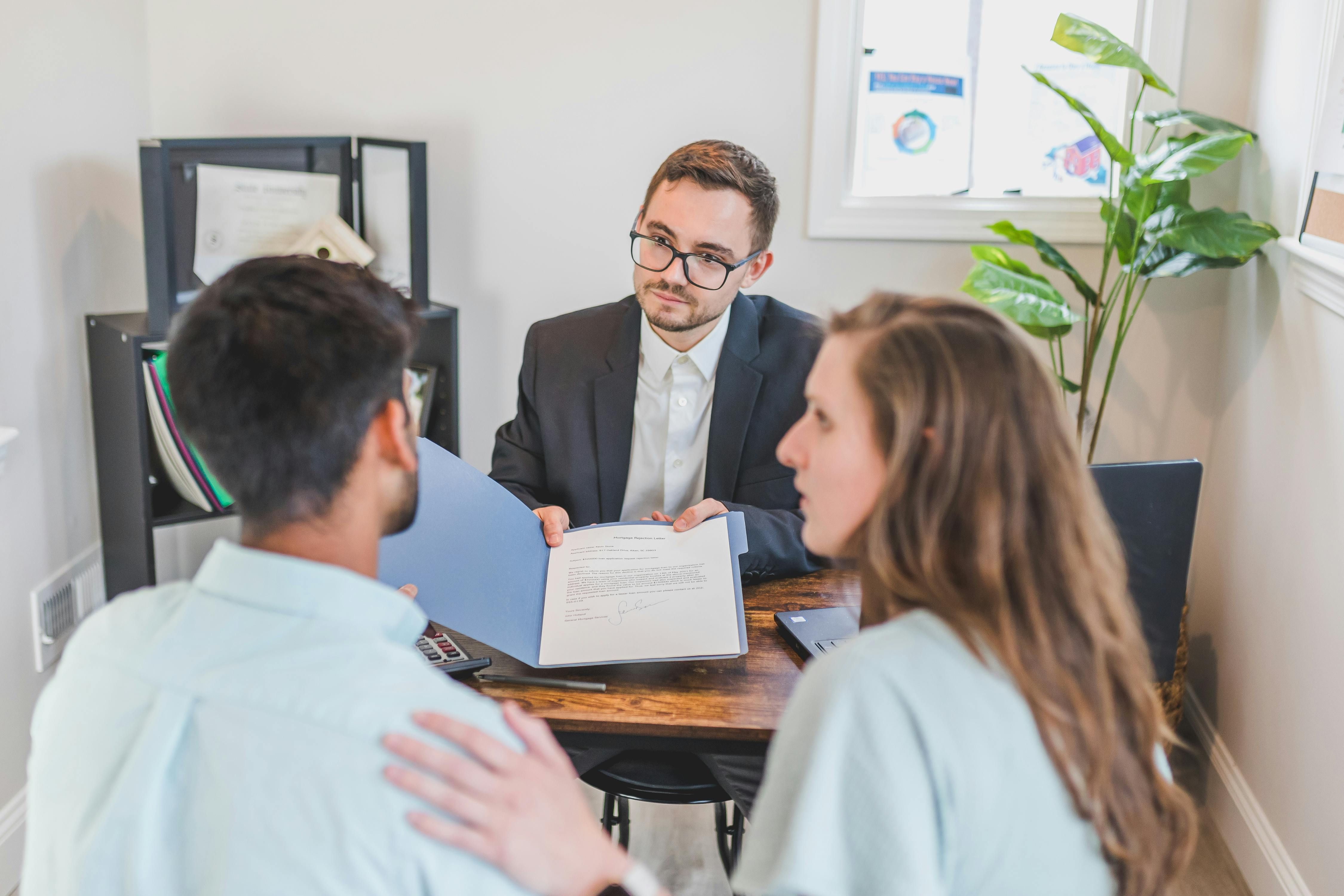 Professional consultant showing document to a young couple in office.