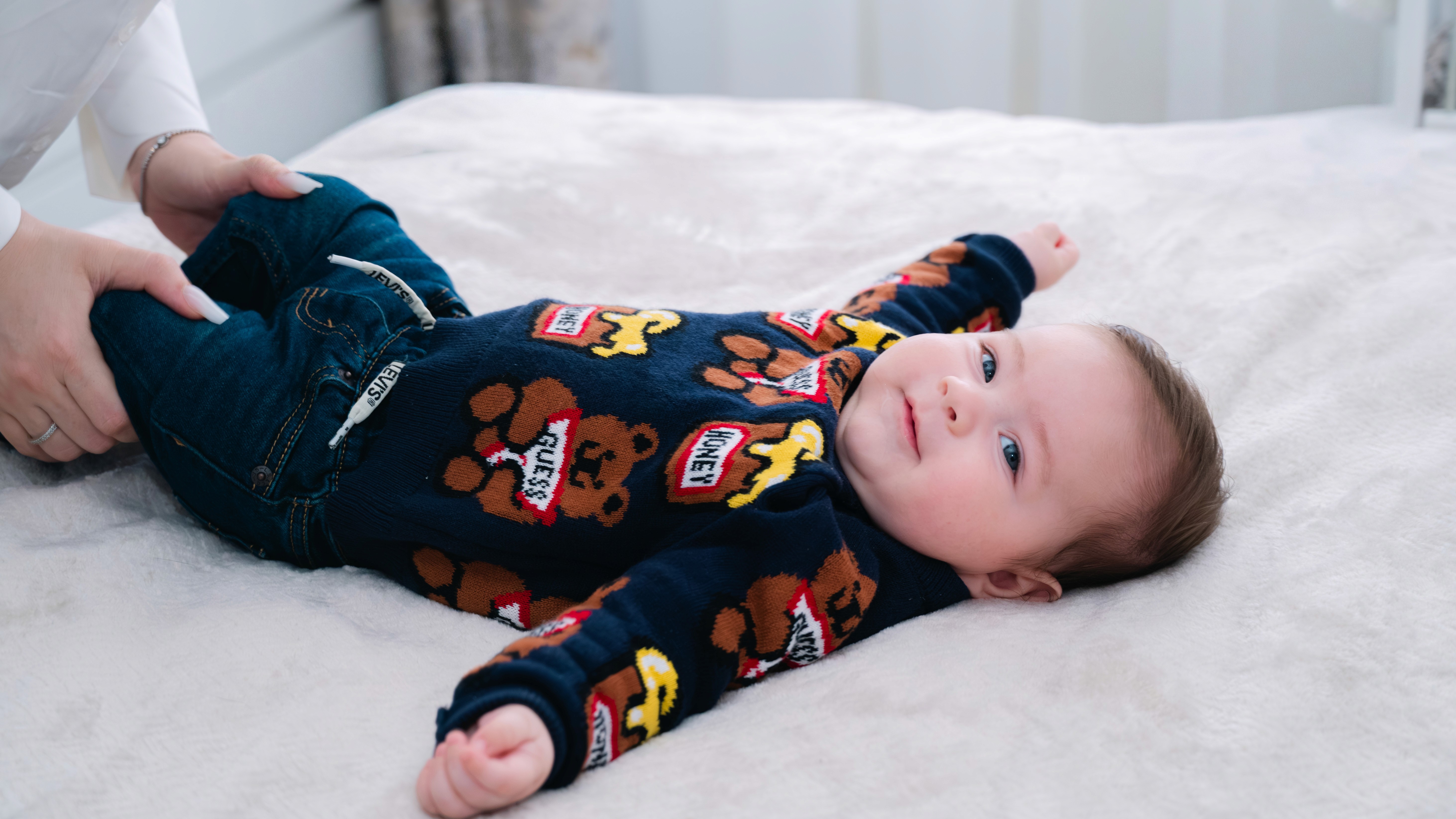 Bebeluș întins pe pat în timpul pregătirilor pentru botez, lumină naturală soft.