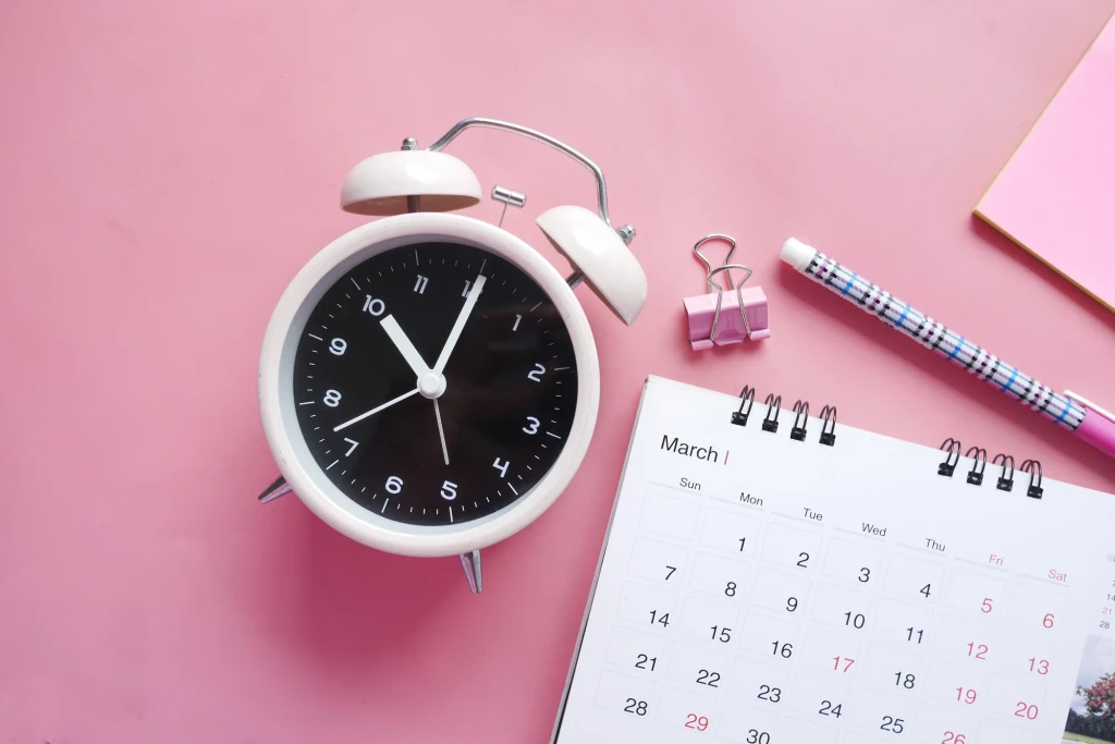 White alarm clock with March calendar and pink office supplies