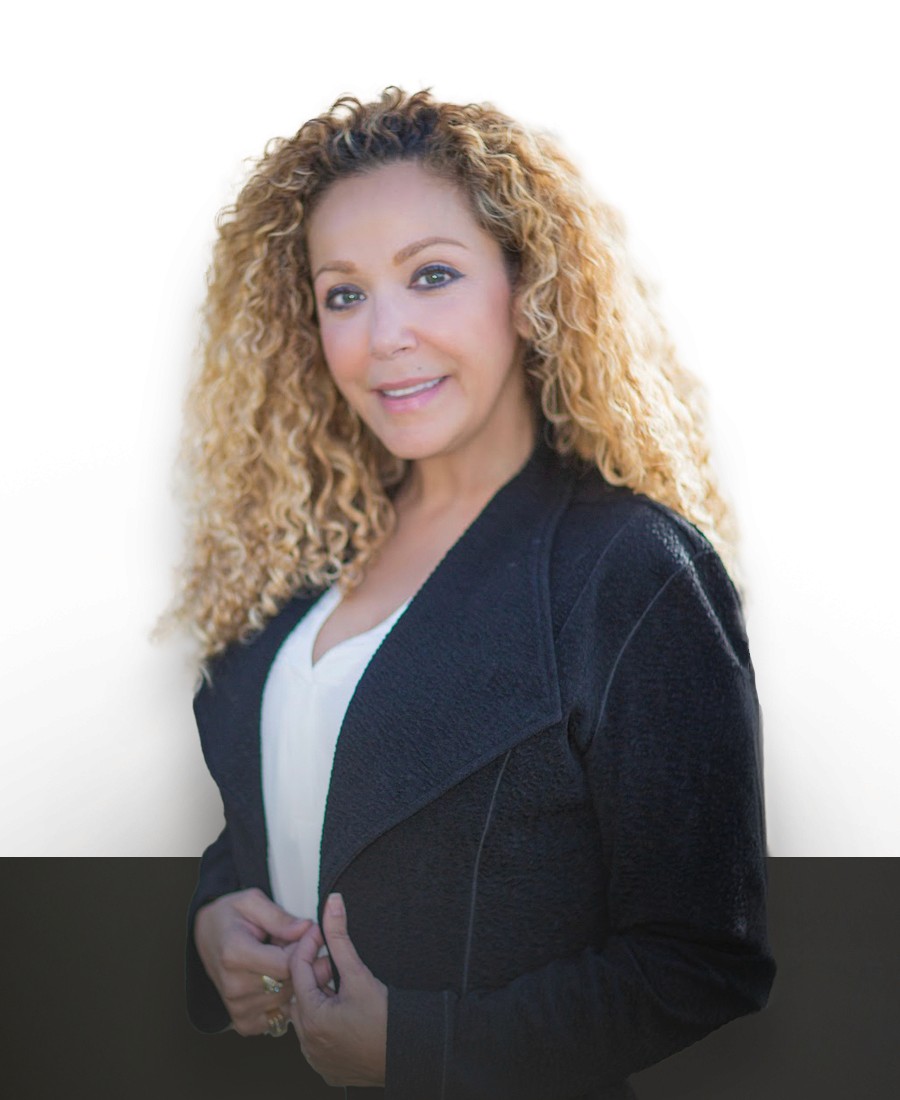 corporate headshot woman with curly brown and blonde hair smiling. Wearing a blue jacket and white shirt.