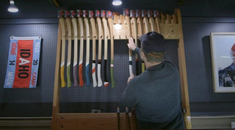 A photo of a man placing some axes on a stand. Each axe has a different colored and styled handle.