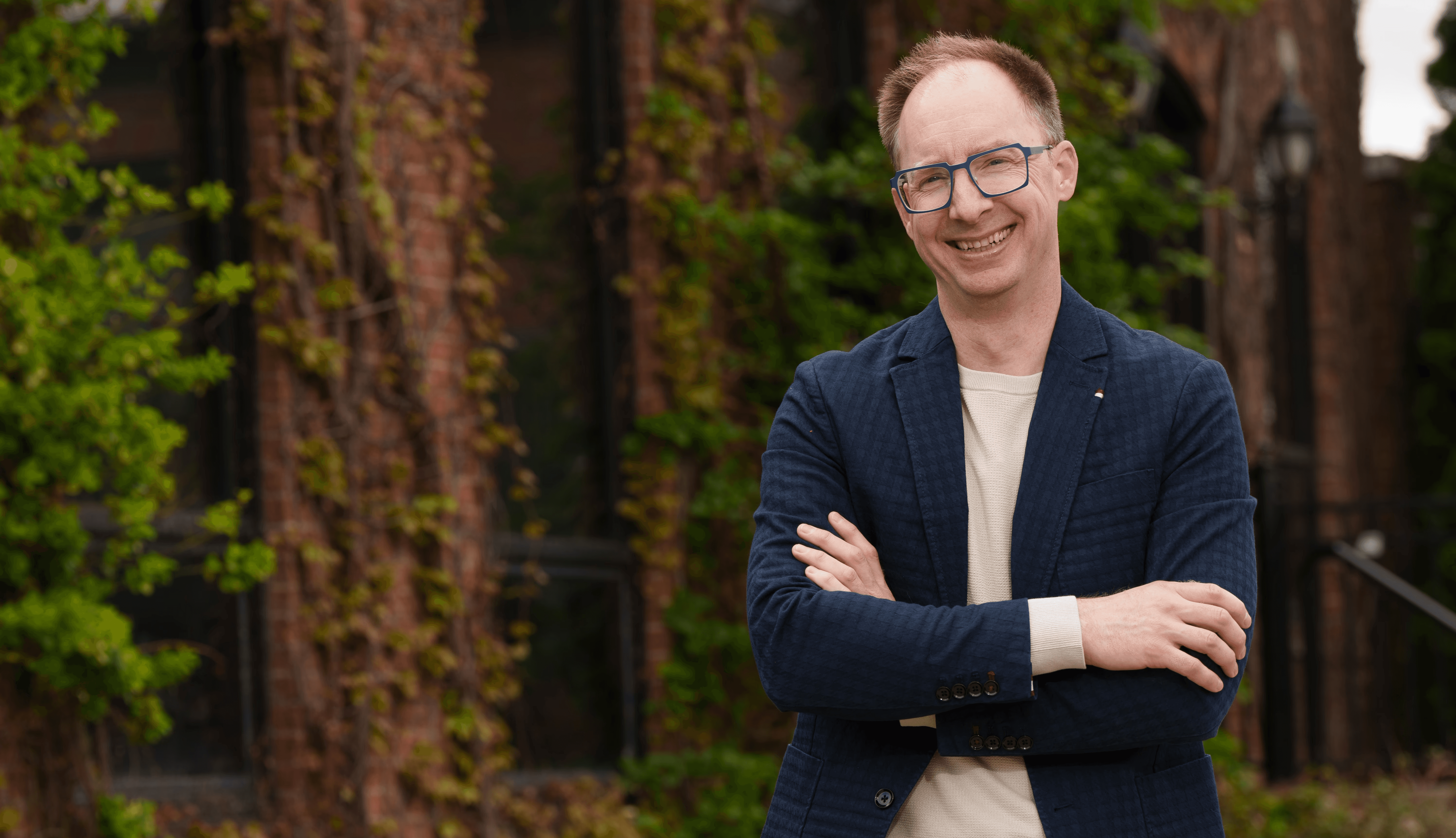 Photo of Cody Hinze. Man in glasses with a suit jacket, arms crossed smiling.