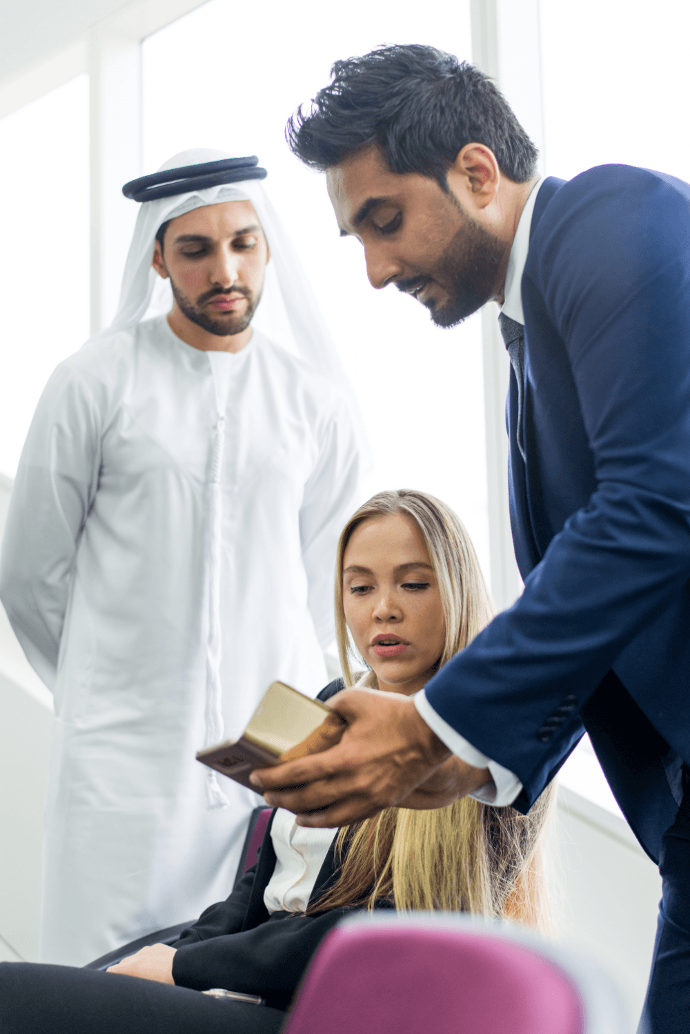 Three professionals engage in a discussion, one showing a phone to a seated woman while another observes.