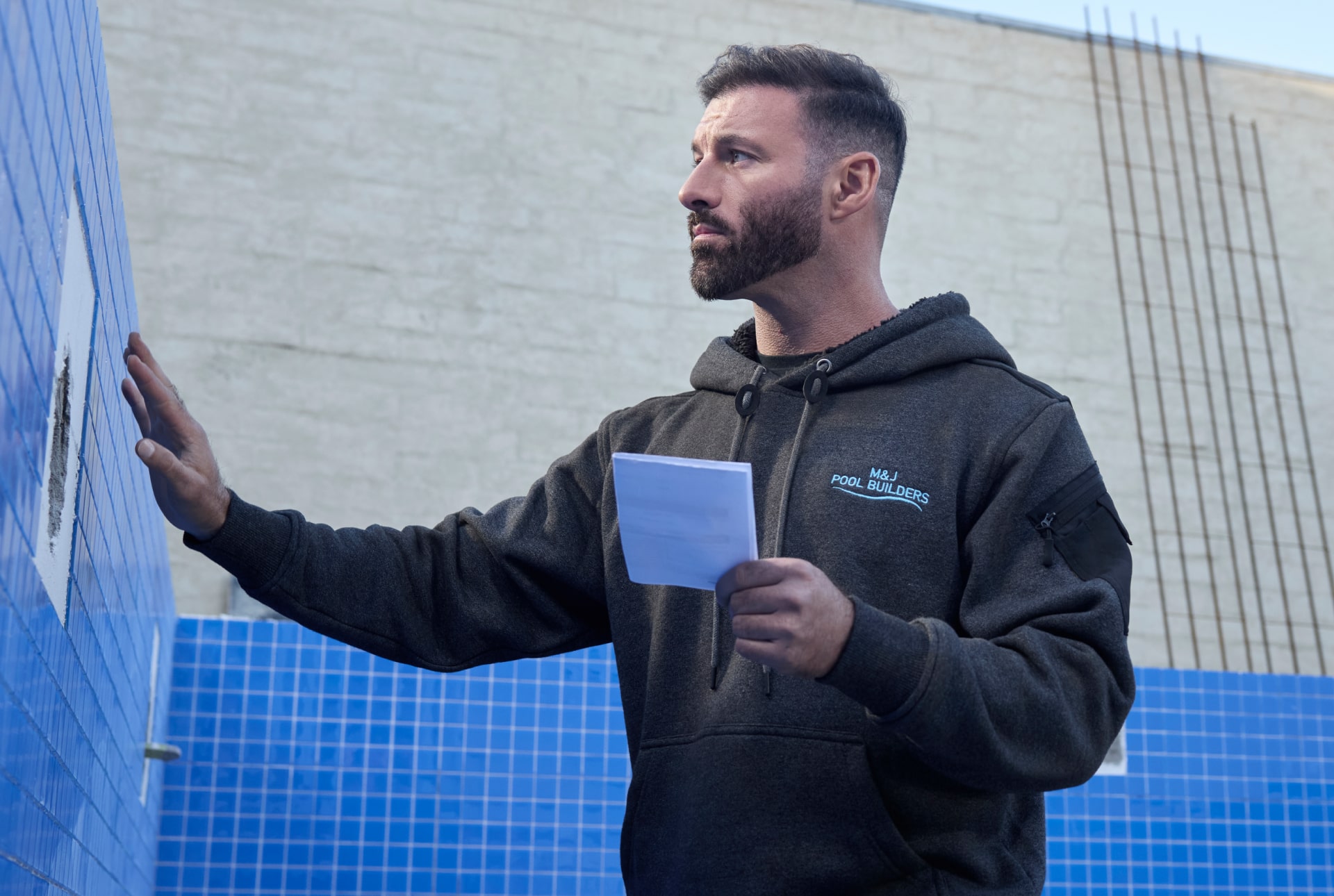 Tradesman standing inside an empty pool holding a tile