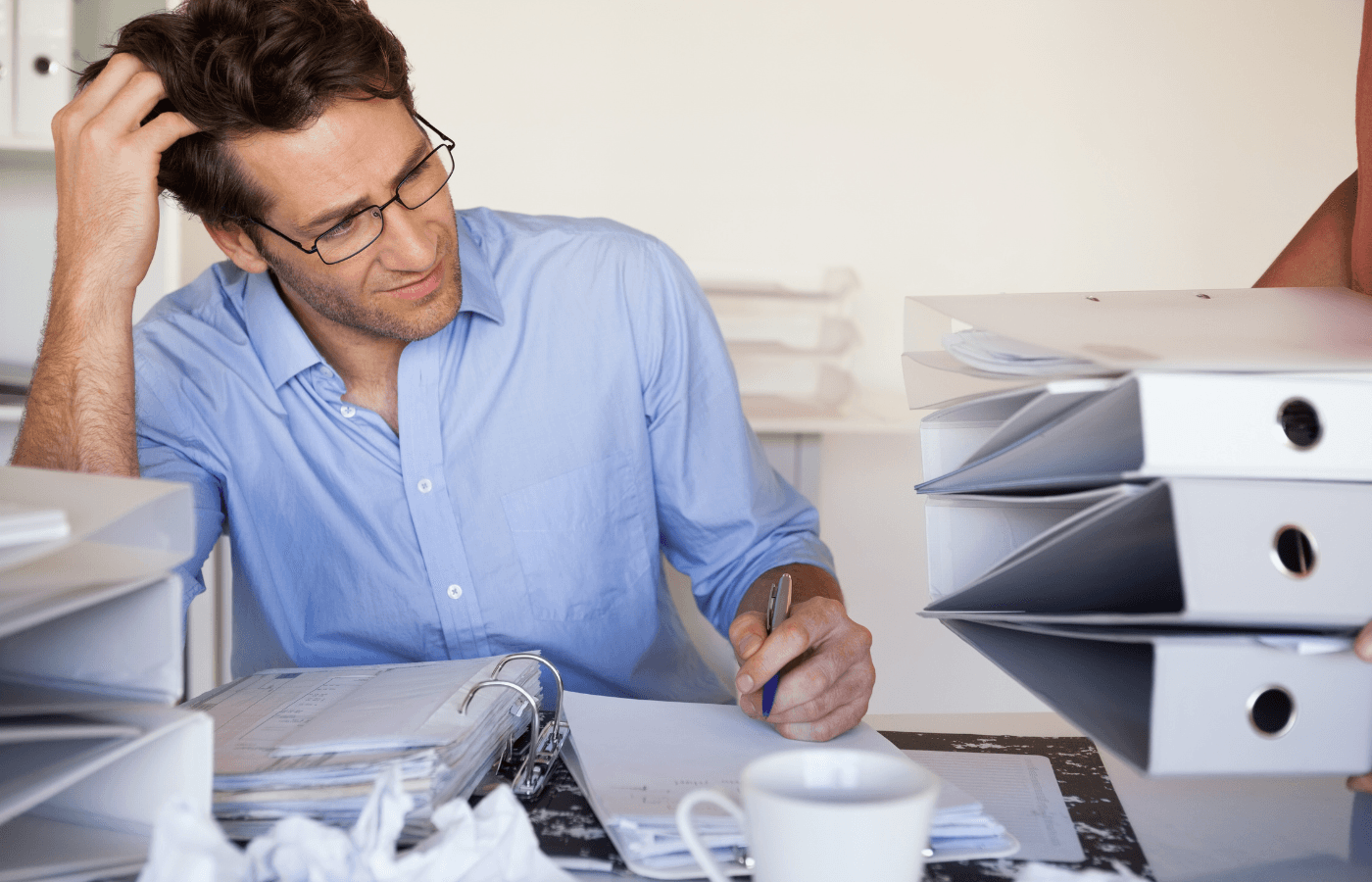 man with piles of paperwork and binders on his desk