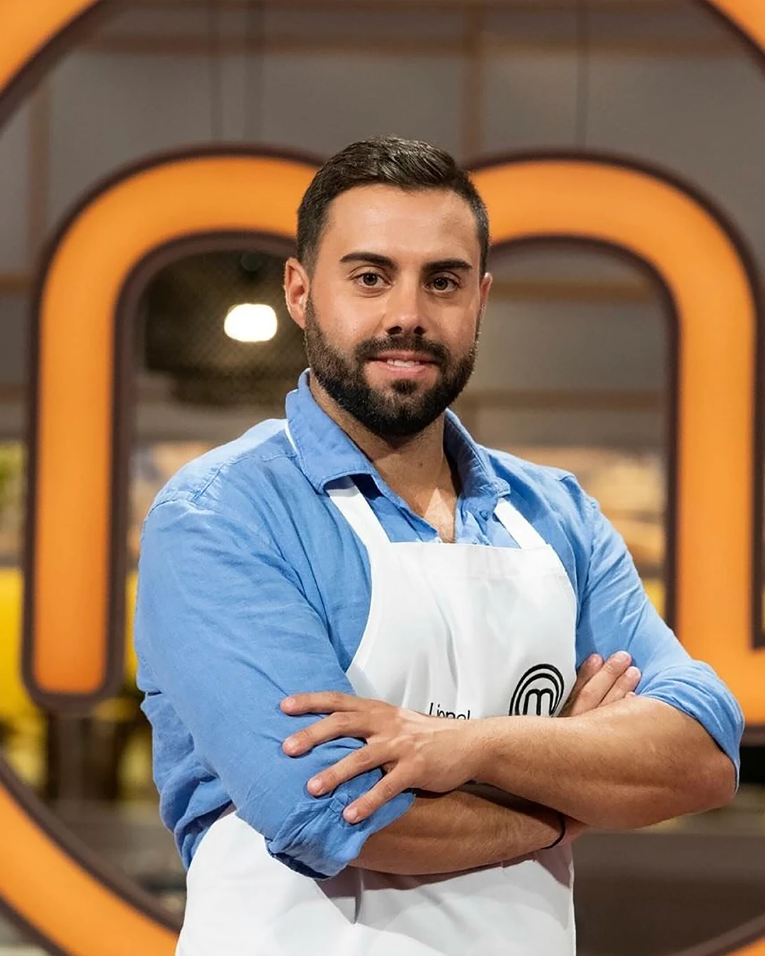A young woman with long dark hair smiles confidently while crossing her arms in a modern indoor setting.