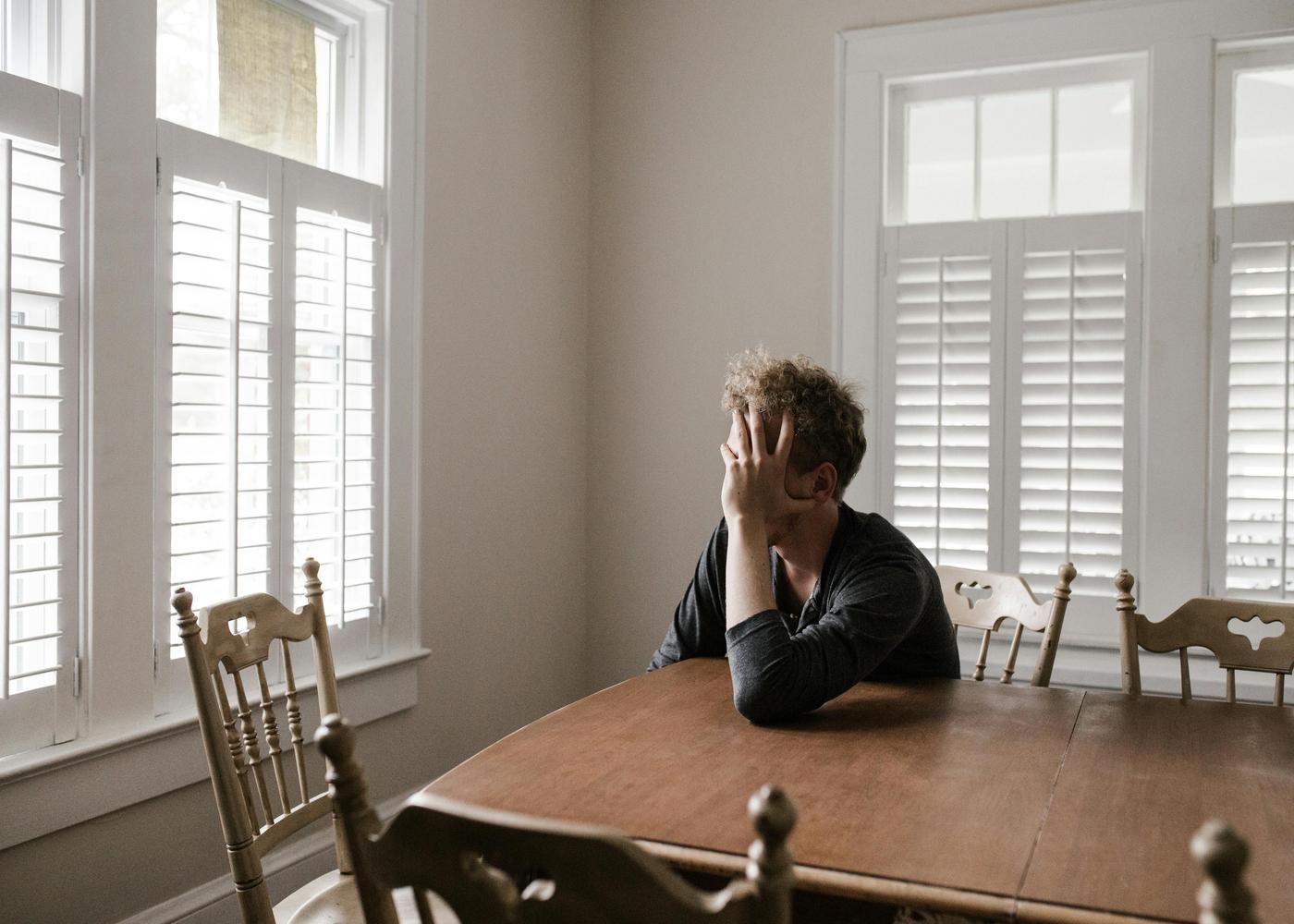 Tired man sitting at a table covering his face with his hand
