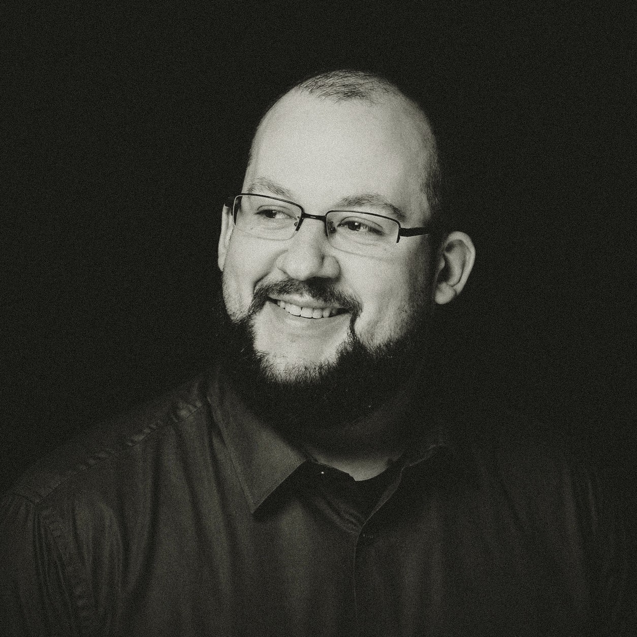 A thoughtful young person with dark hair gazes to the side, captured in soft black and white lighting.