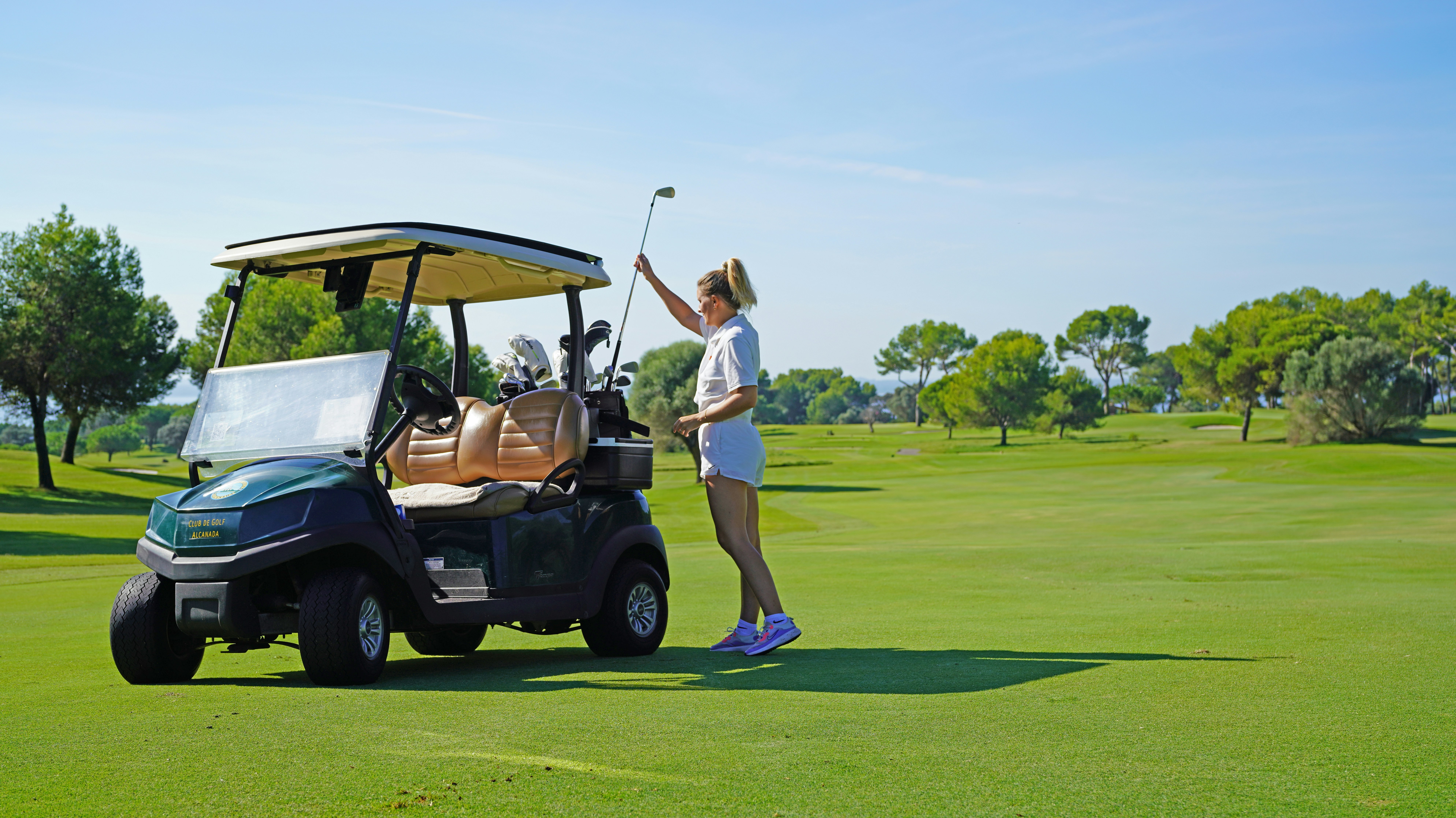 A woman standing next to a golf cart on a golf course