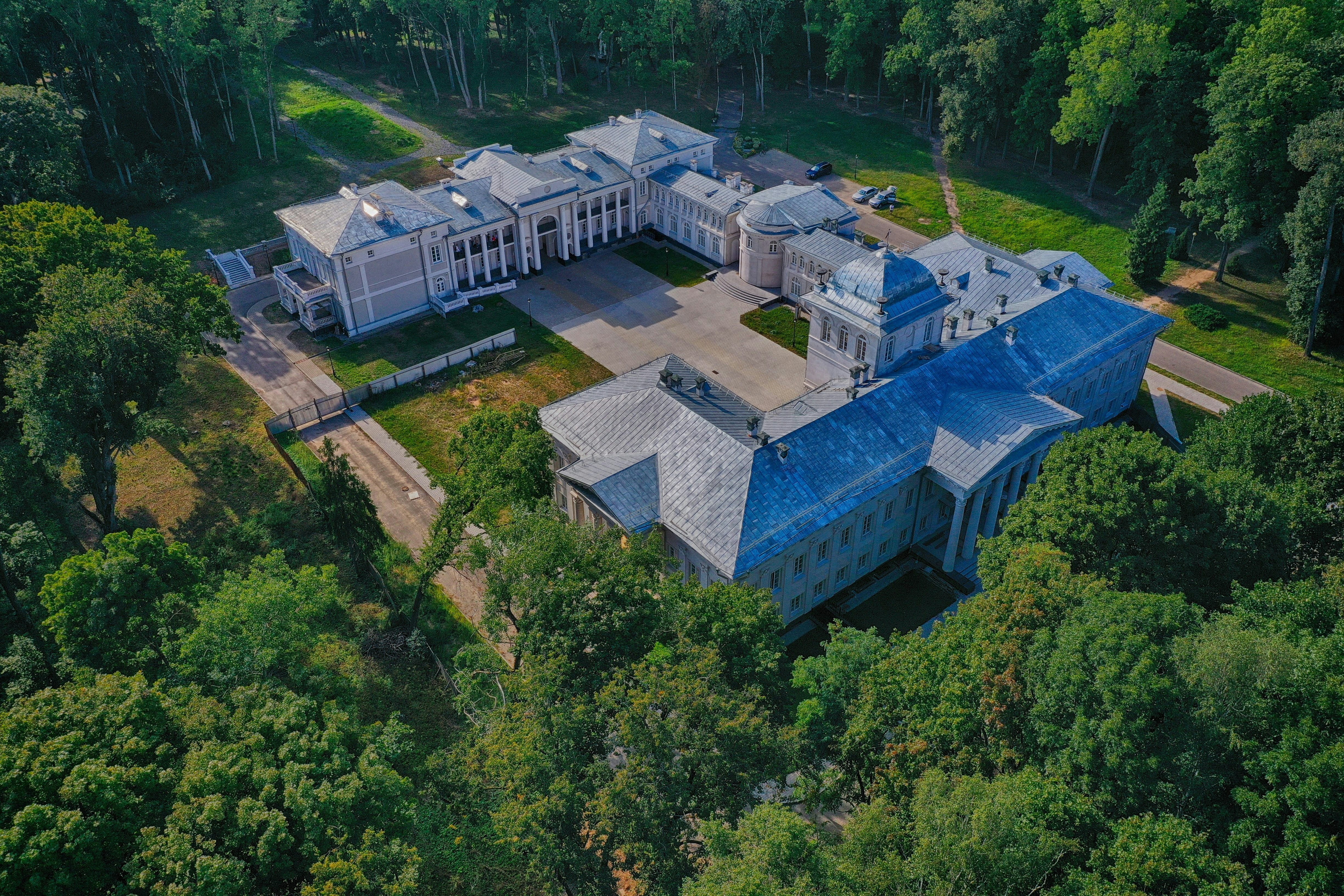 An expansive estate surrounded by lush trees, featuring a large, elegant mansion with a blue roof.