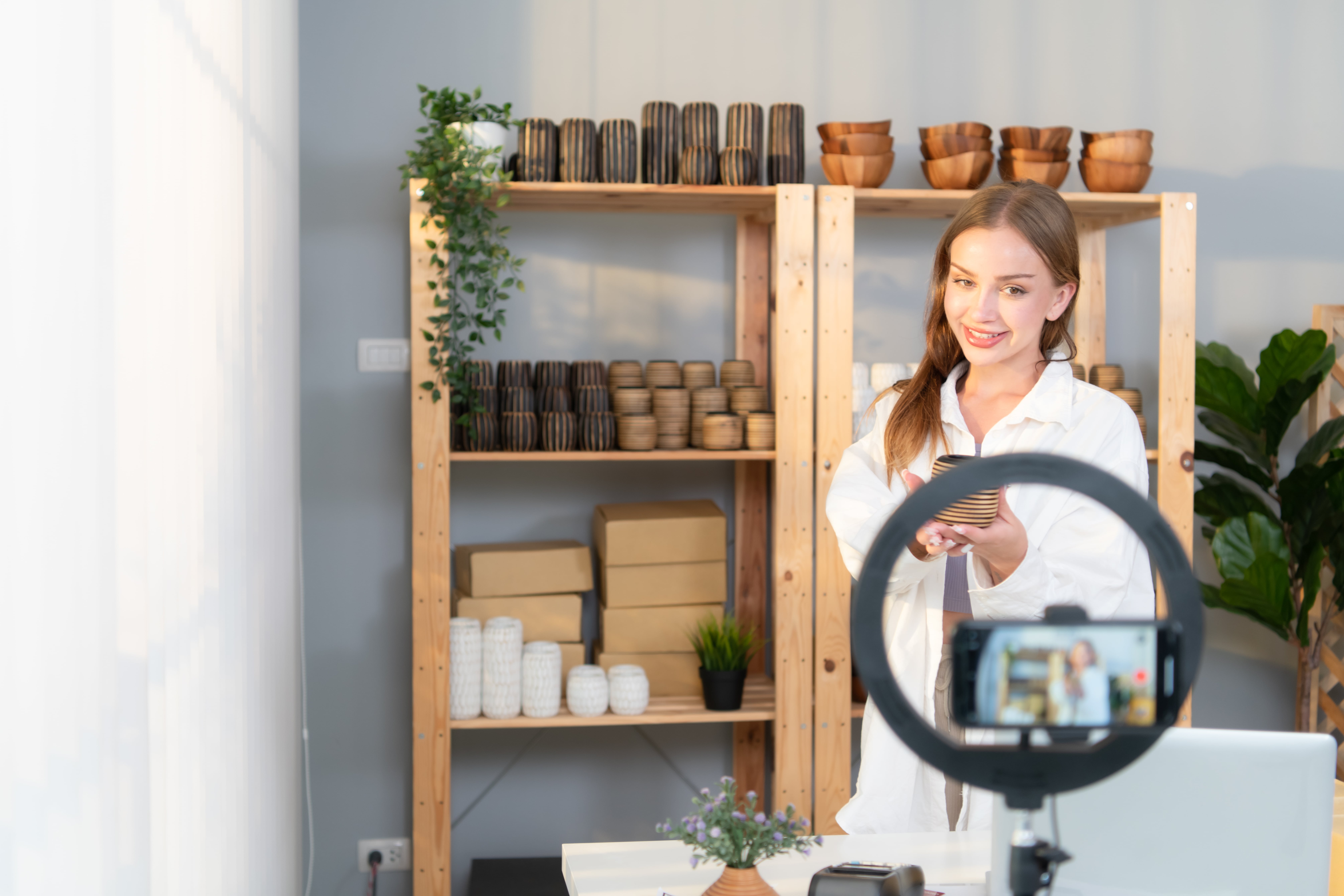 Young female entrepreneur showcasing handcrafted products in front of a ring light camera setup for product photography and online selling.