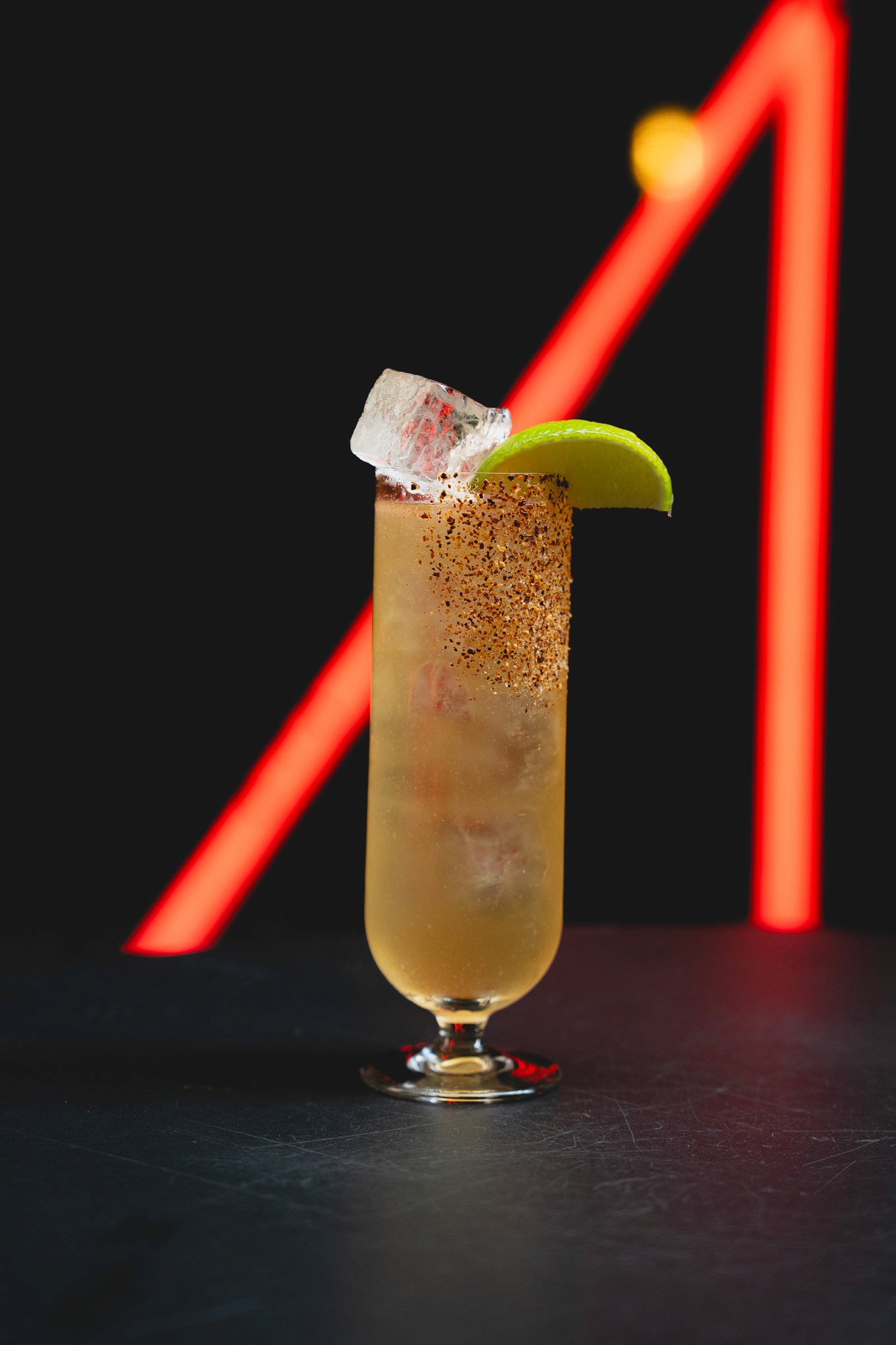 White plate with roasted carrots served on green sauce, topped with almonds and fresh herbs, held by a hand over a dark table.