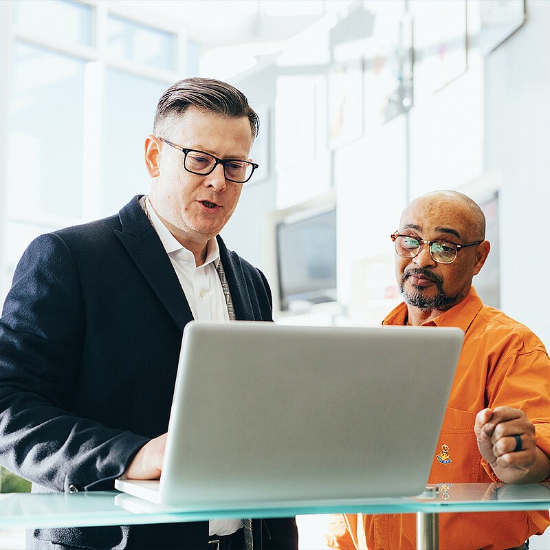 Woman with a short haircut smiling confidently, wearing a blazer and standing in warm natural light with modern architecture behind her.