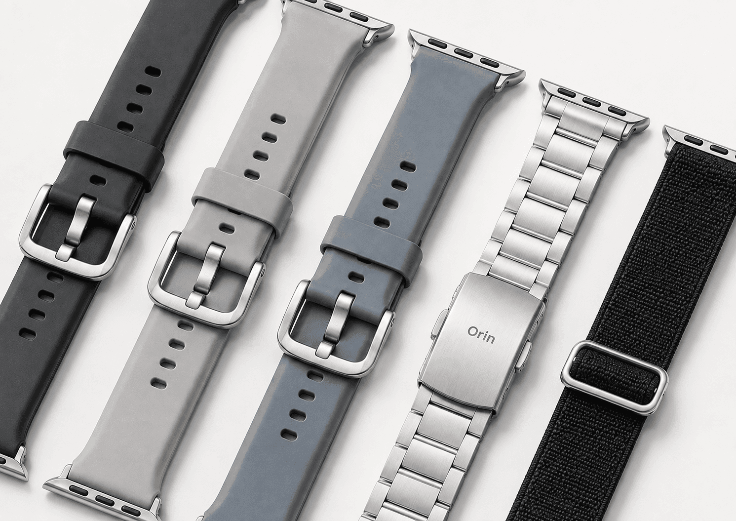Flat lay of Orin watch straps — silicone, brushed steel and woven fabric bands in black, grey and slate