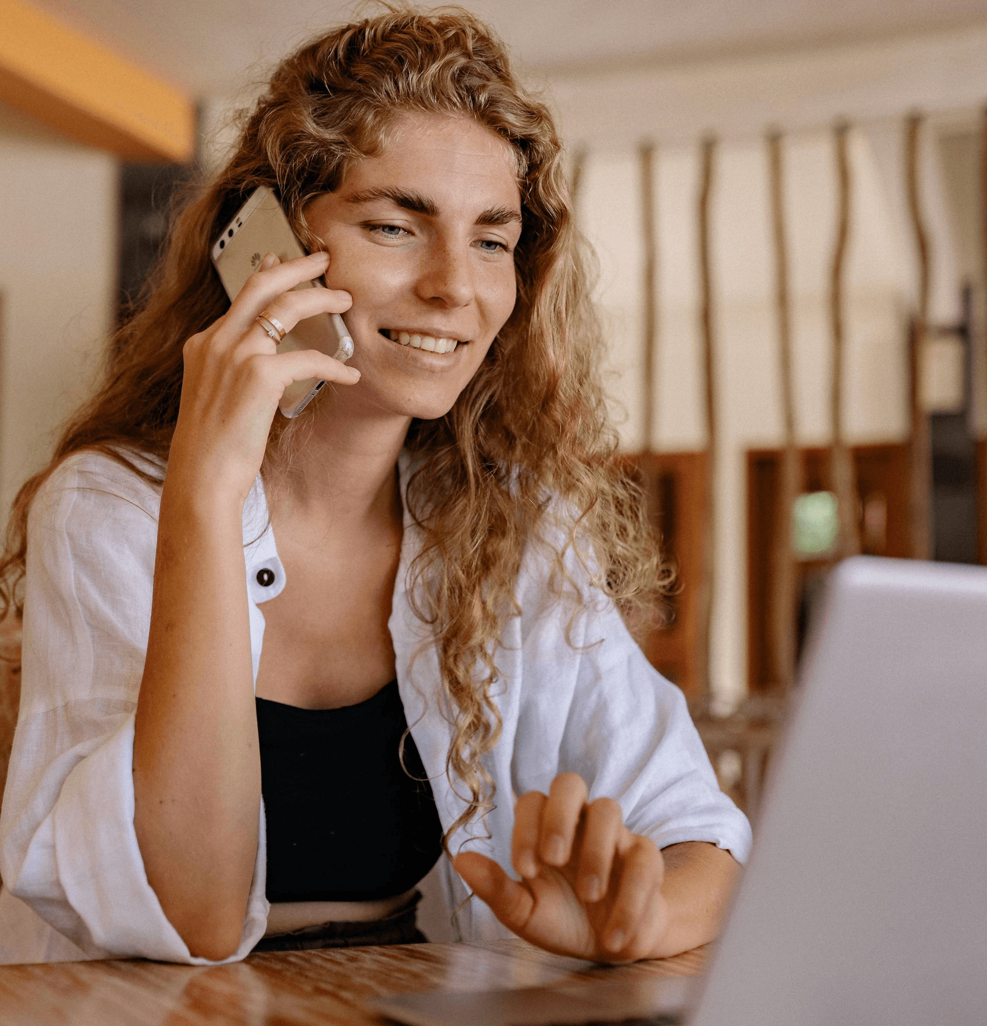 A woman holding a phone on a laptop smiling