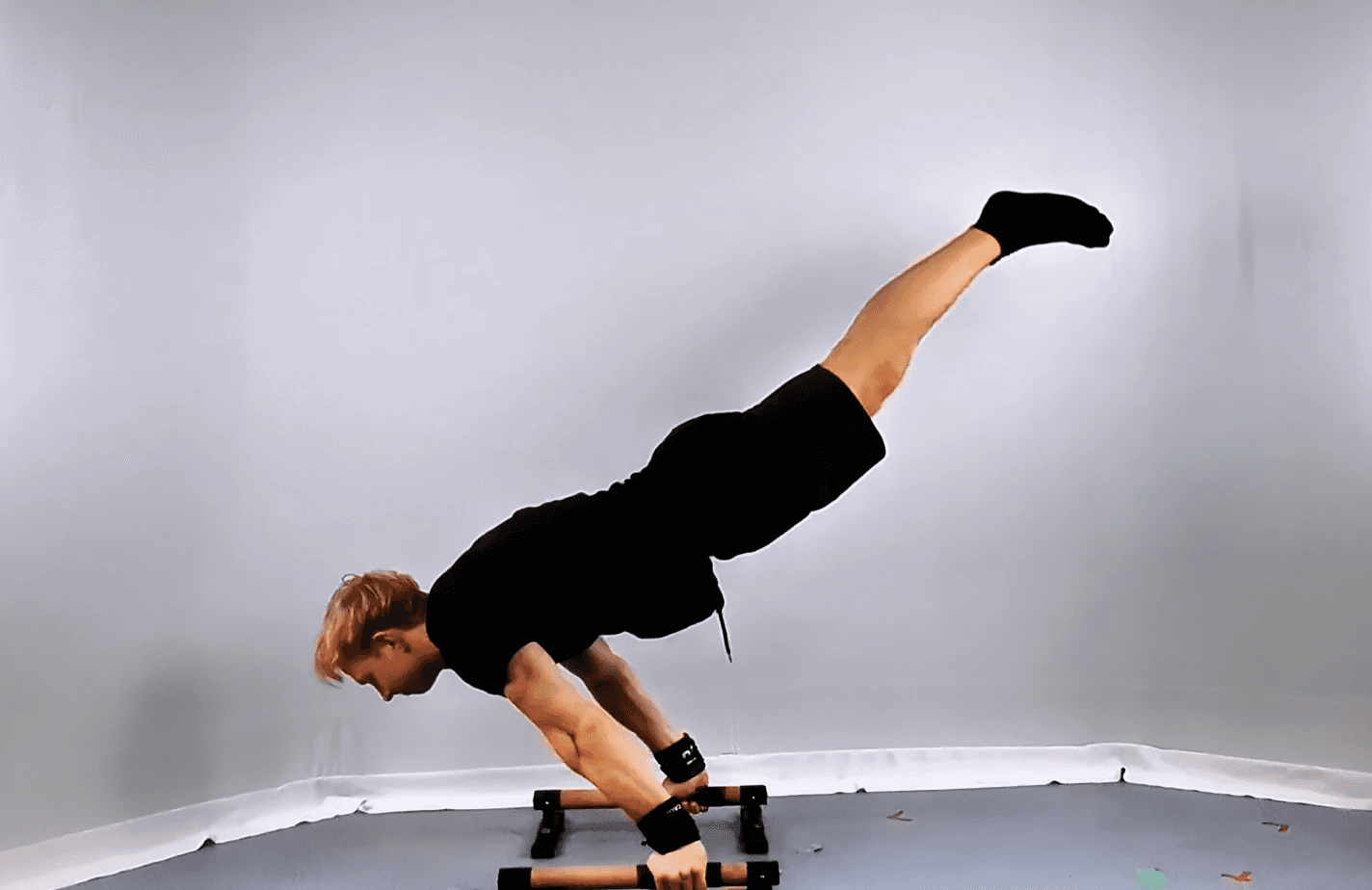 A person demonstrates impressive strength and balance while transitioning from a full planche to a handstand with momentum on parallel bars, in a minimalist indoor setting.