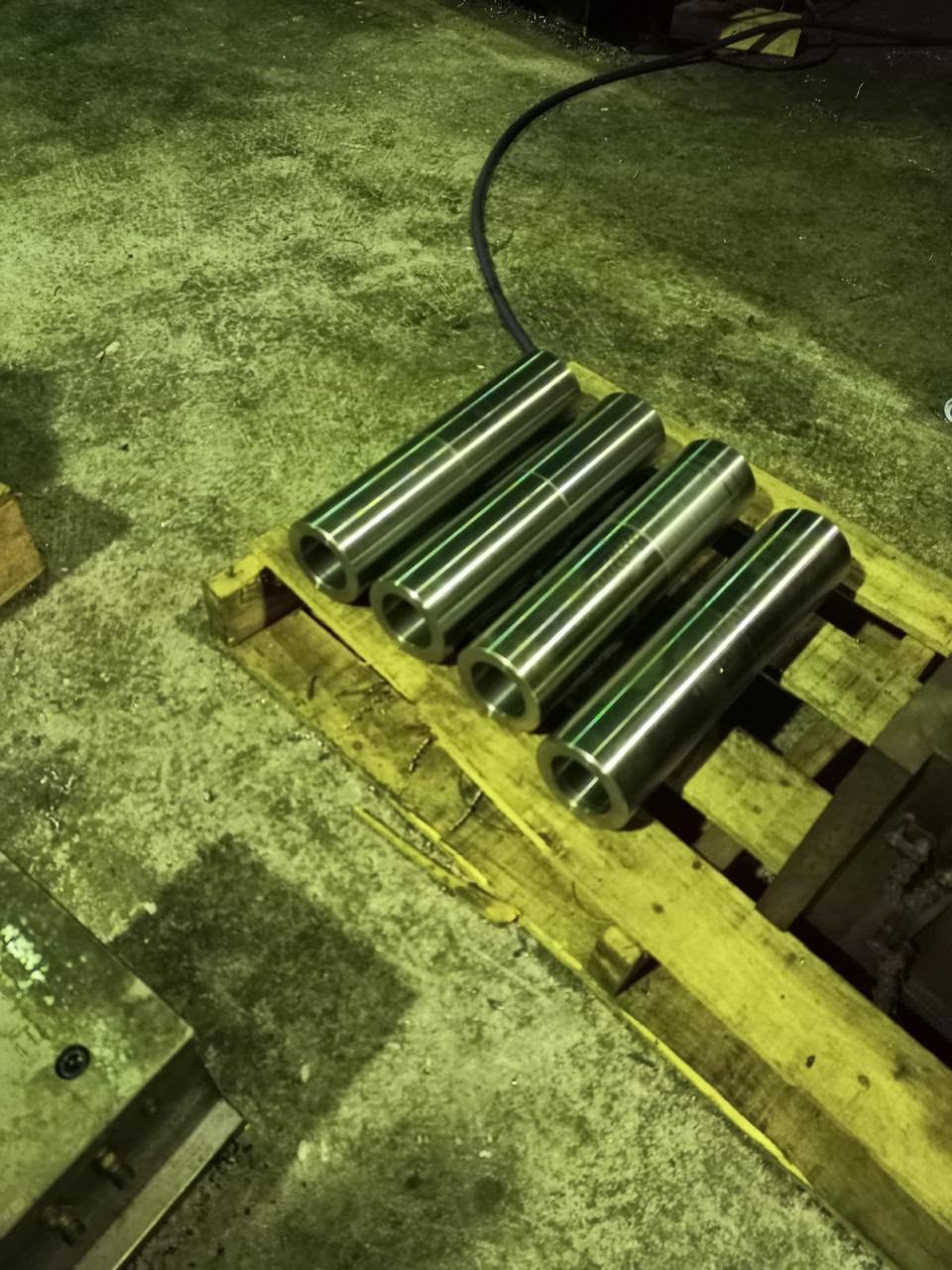 A set of four finished, heavy-duty metal cylindrical shafts arranged on a wooden shipping pallet.