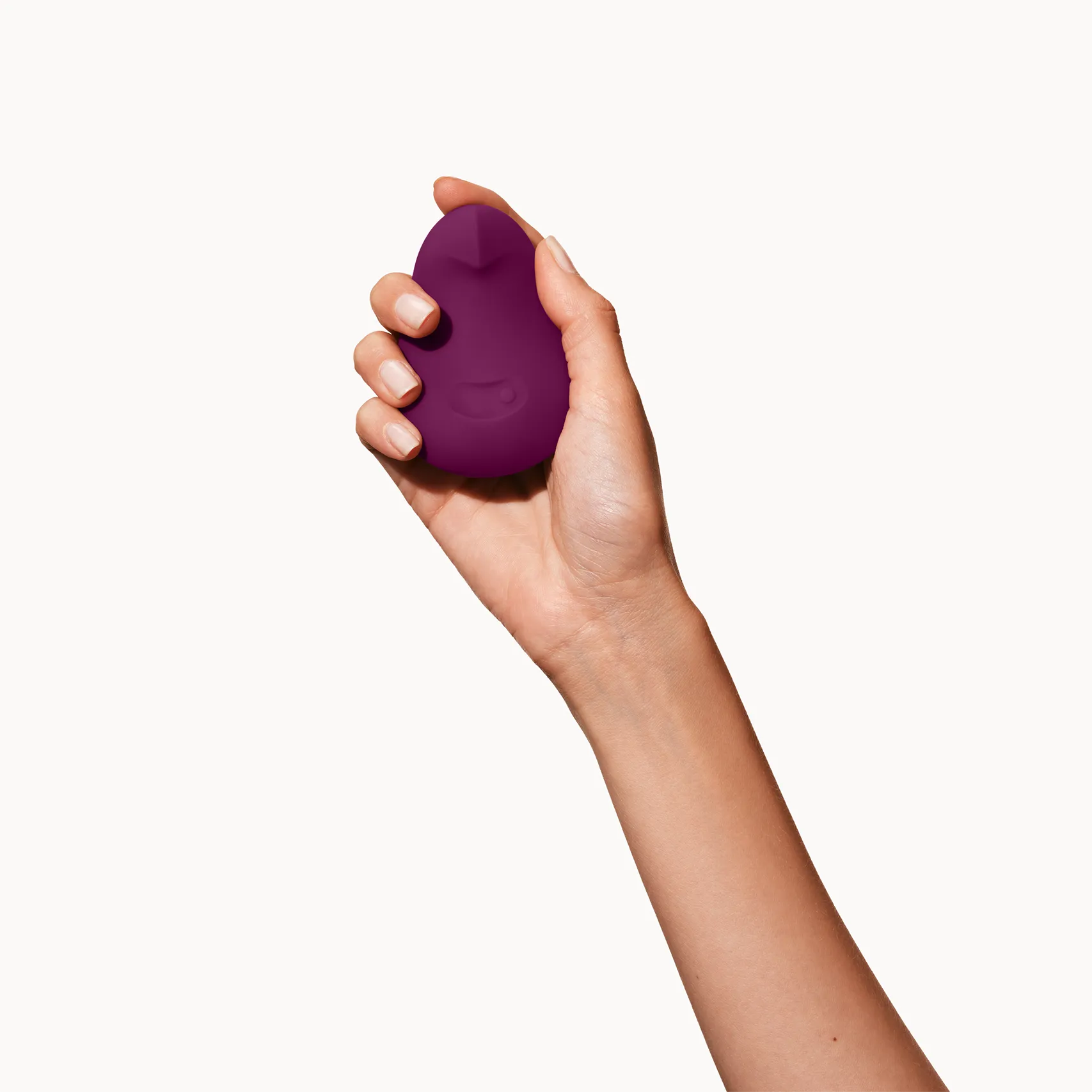 Hand holding a purple Dame Pom sexual wellness device on a white background
