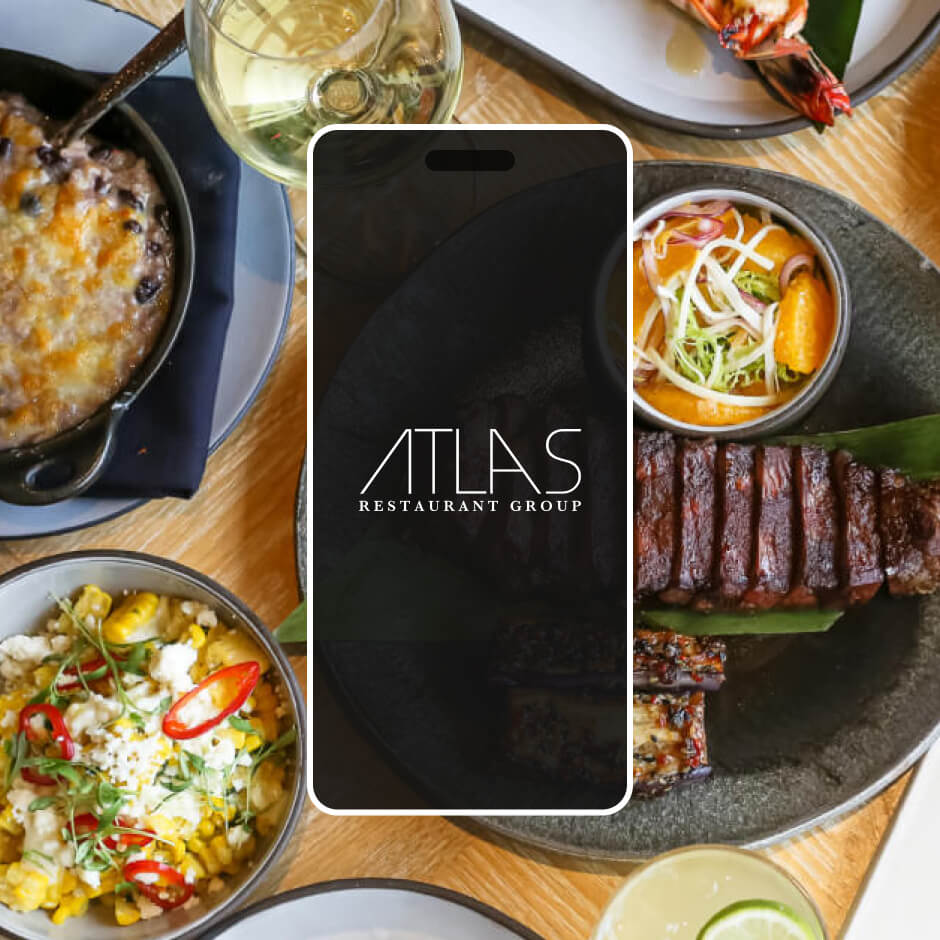 A table set with various plated dishes, including grilled steak, casserole, vegetables, a glass of white wine, and a phone displaying the Atlas Restaurant Group logo.