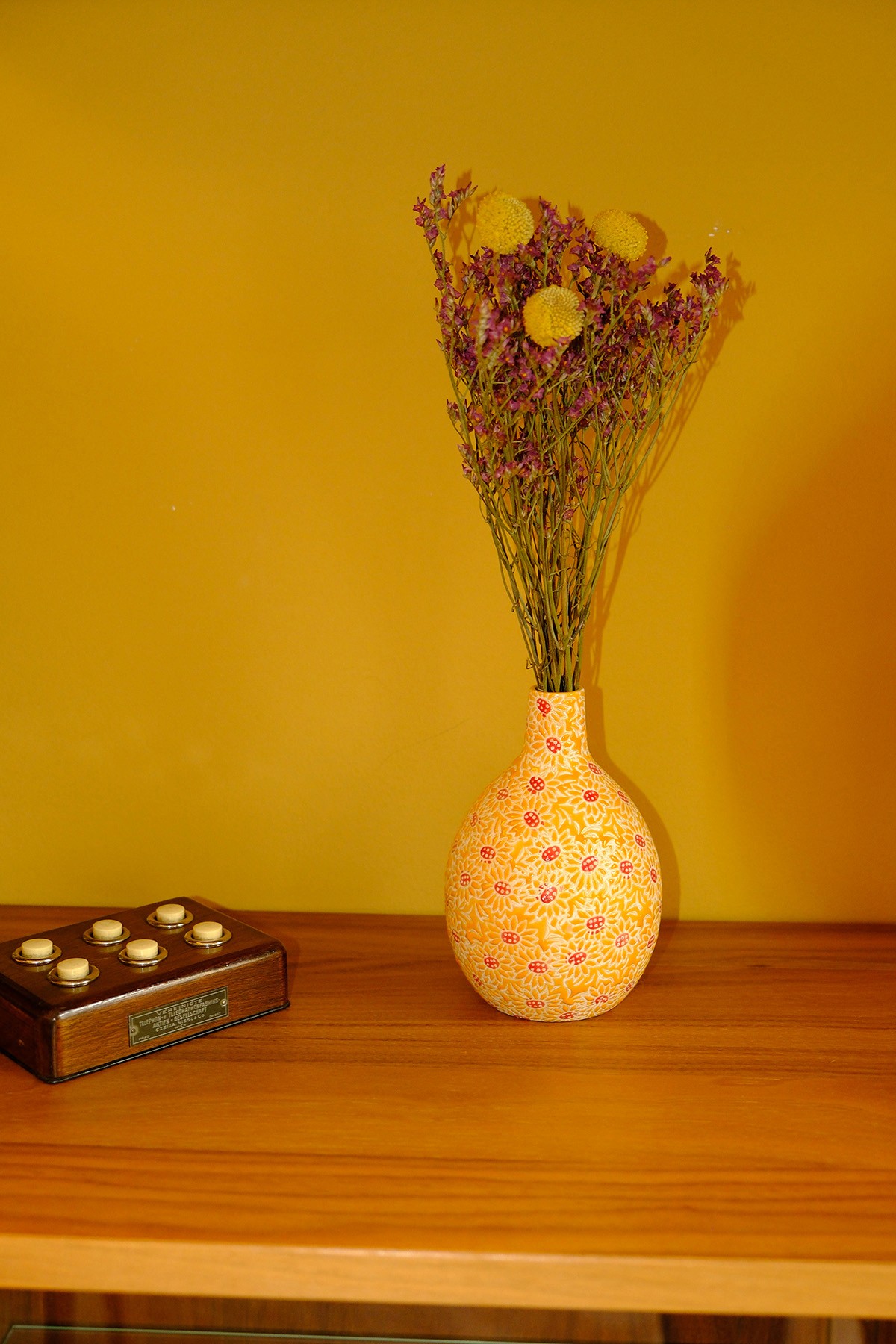 Bunte Vase mit Trockenblumen vor gelber Wand