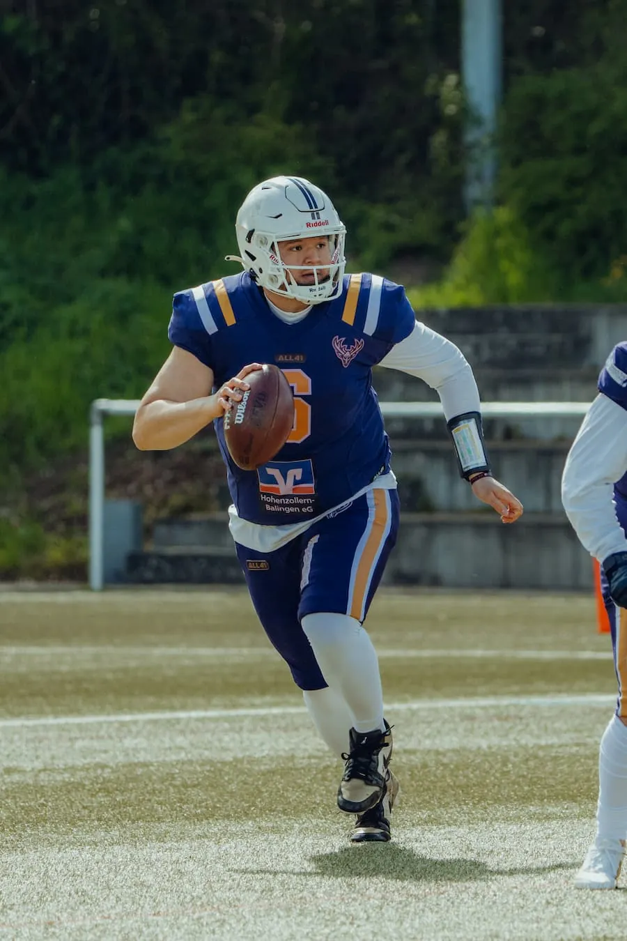 Der Quarterback der Bucks im blauen Trikot läuft mit dem Ball in der Hand und schaut nach vorn.