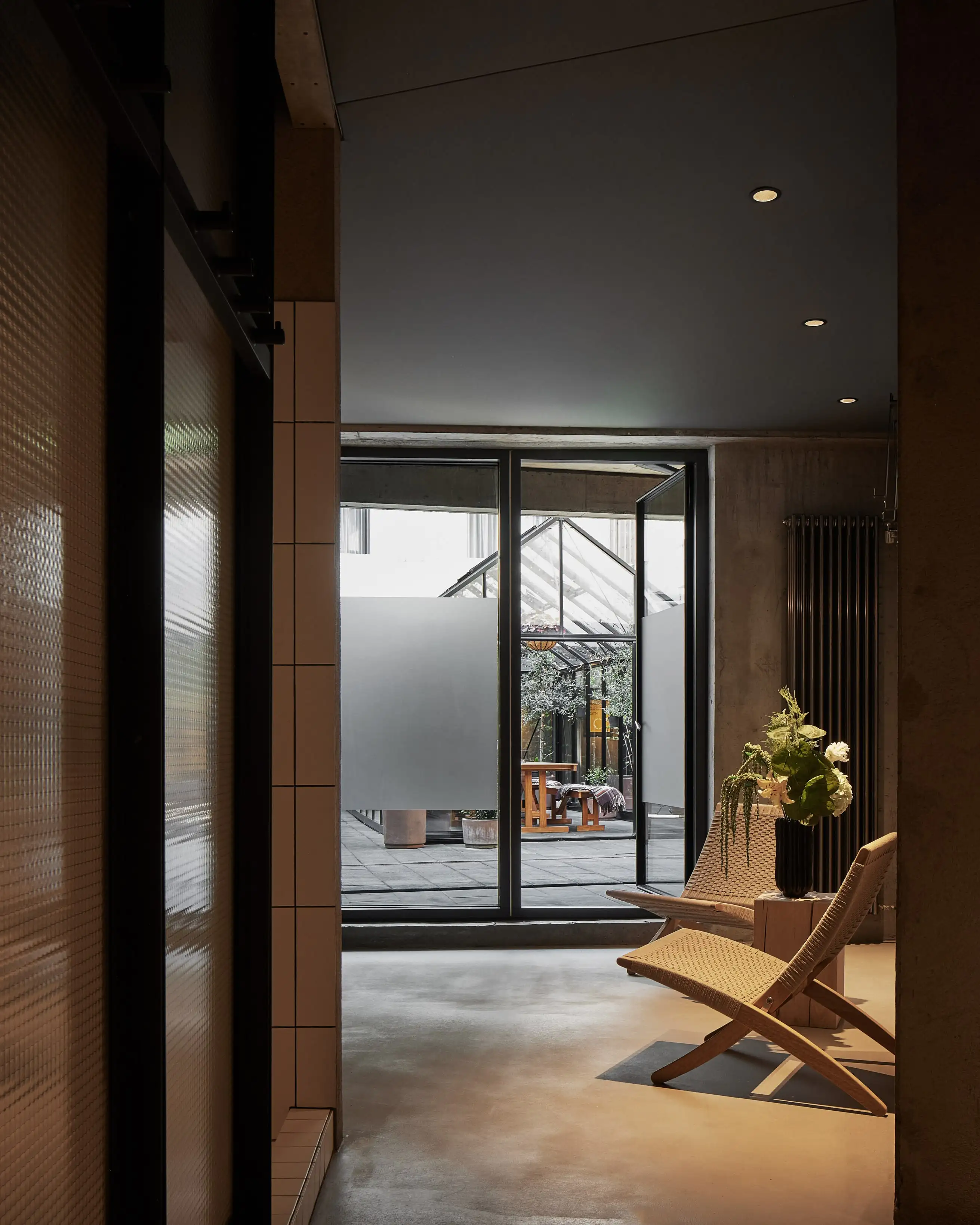Hallway view into the glasshouse courtyard with a woven lounge chair