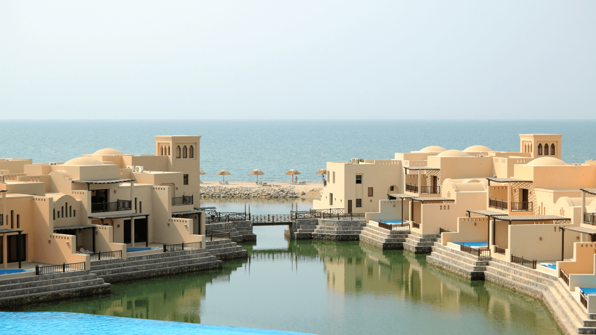 Seaside resort architecture with beige villas reflected on calm water under a clear sky, symbolizing hospitality development and design excellence | Lunasole Hospitality