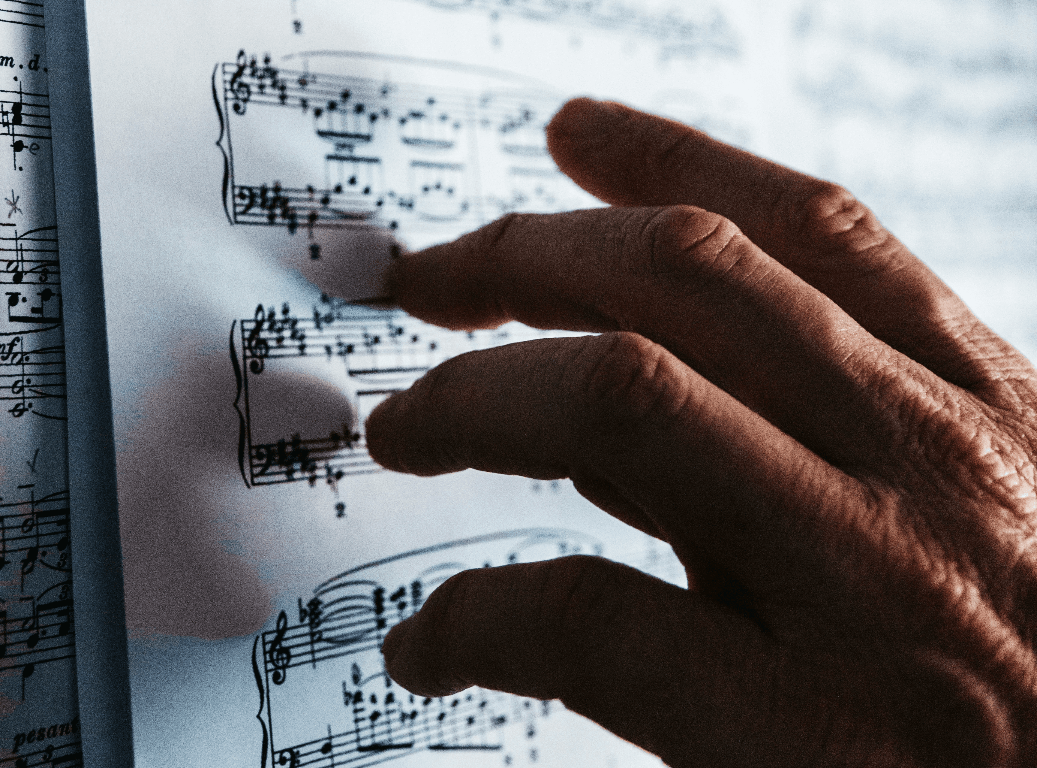 A wizened hand scrolling over sheet music arrangements. Photo by Isaac Ibbott on Unsplash