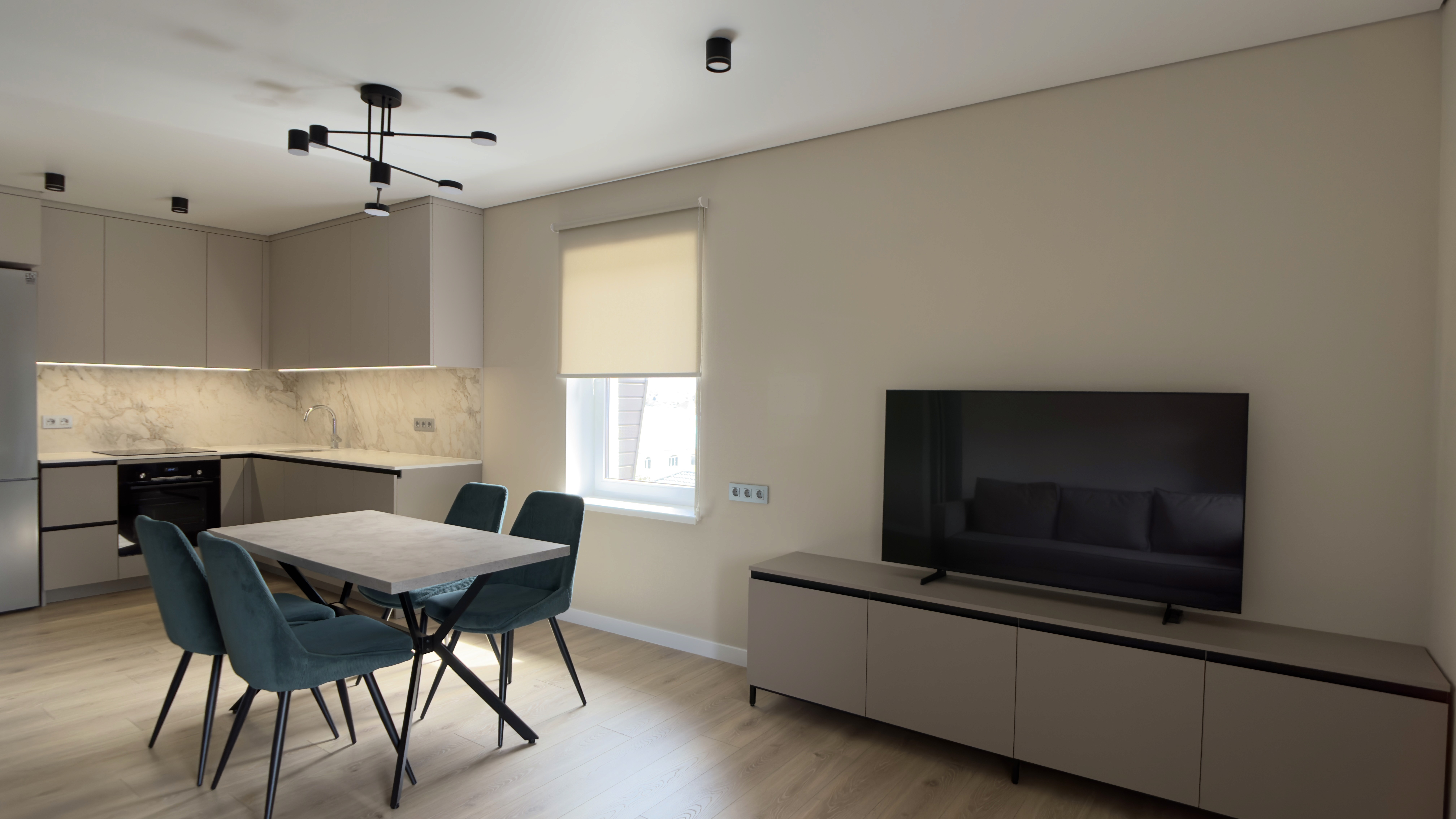 Інтер’єр вітальні з кухнею, телевізором і сучасними меблями у світлих тонах