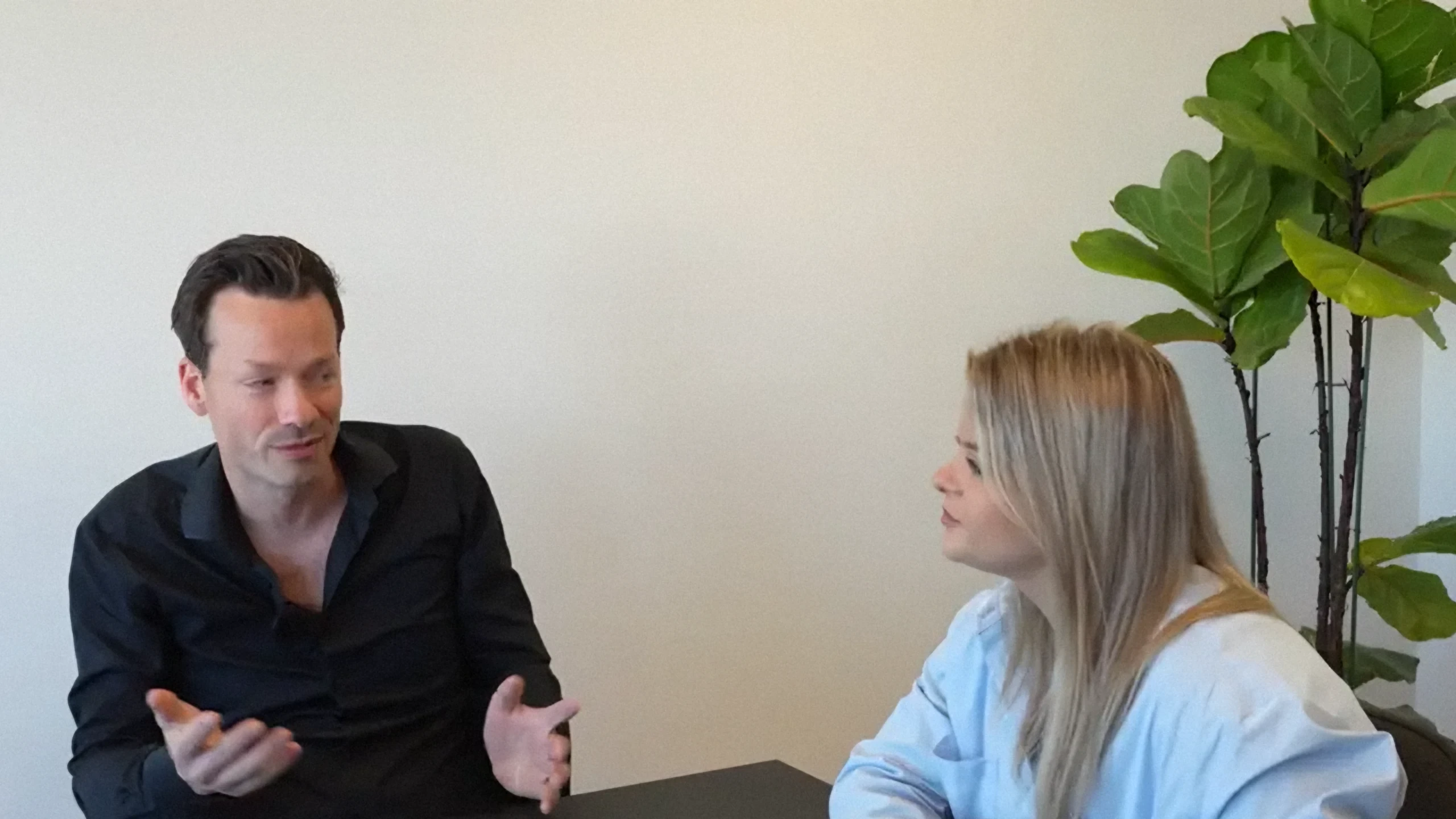 Twee gesprekspartners aan tafel in een lichte ruimte met een plant, tijdens een experttalk