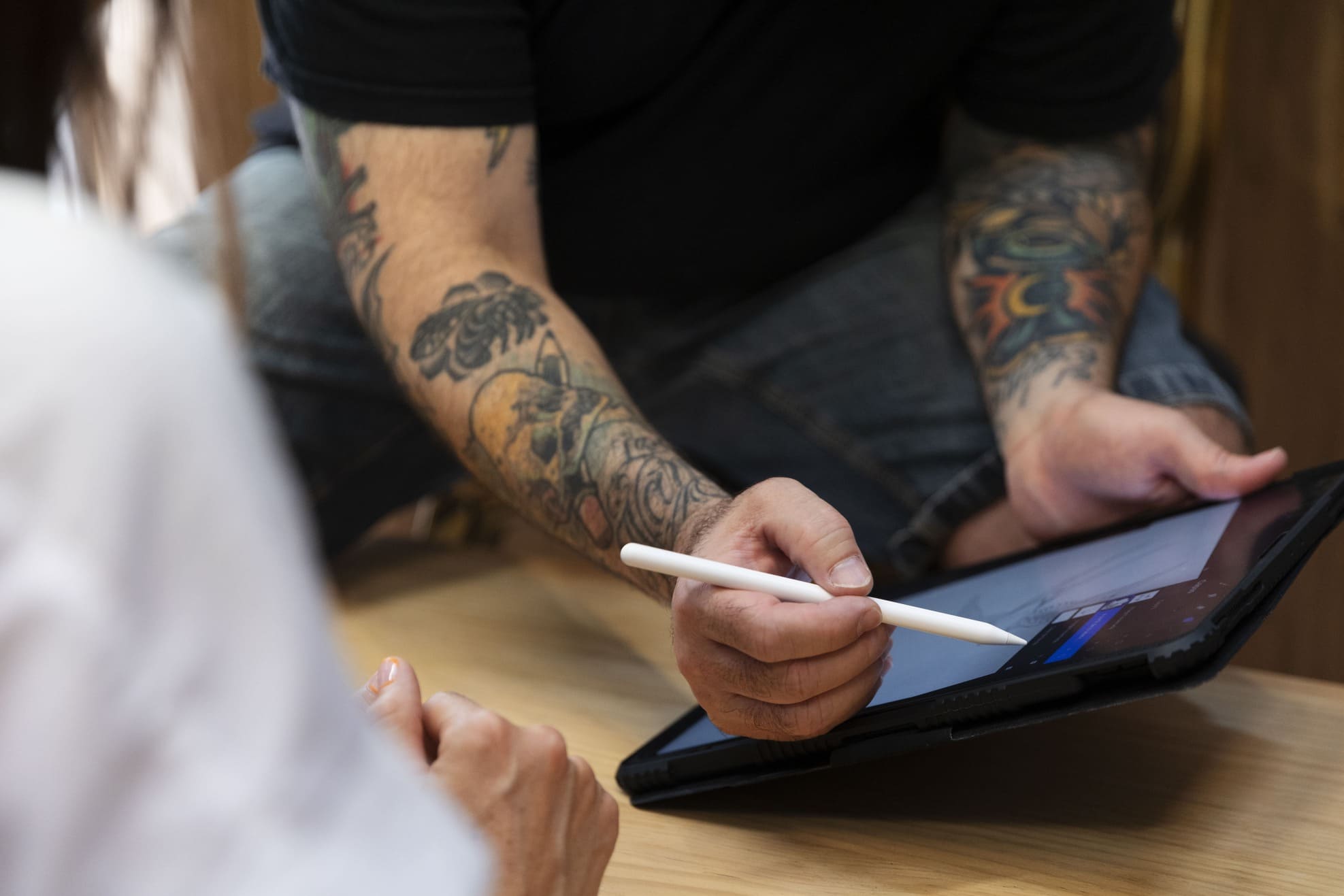 Tattoo artist and client discussing tattoo template on tablet