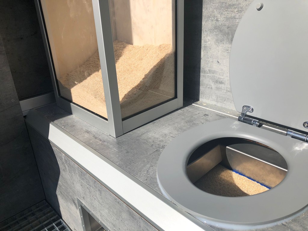 Reell Foto vun der NoWaSan dréchen Toilette vun bannen, déi d'Innenausstattung an technesch Detailer vun der waasserloser Funktioun weist.