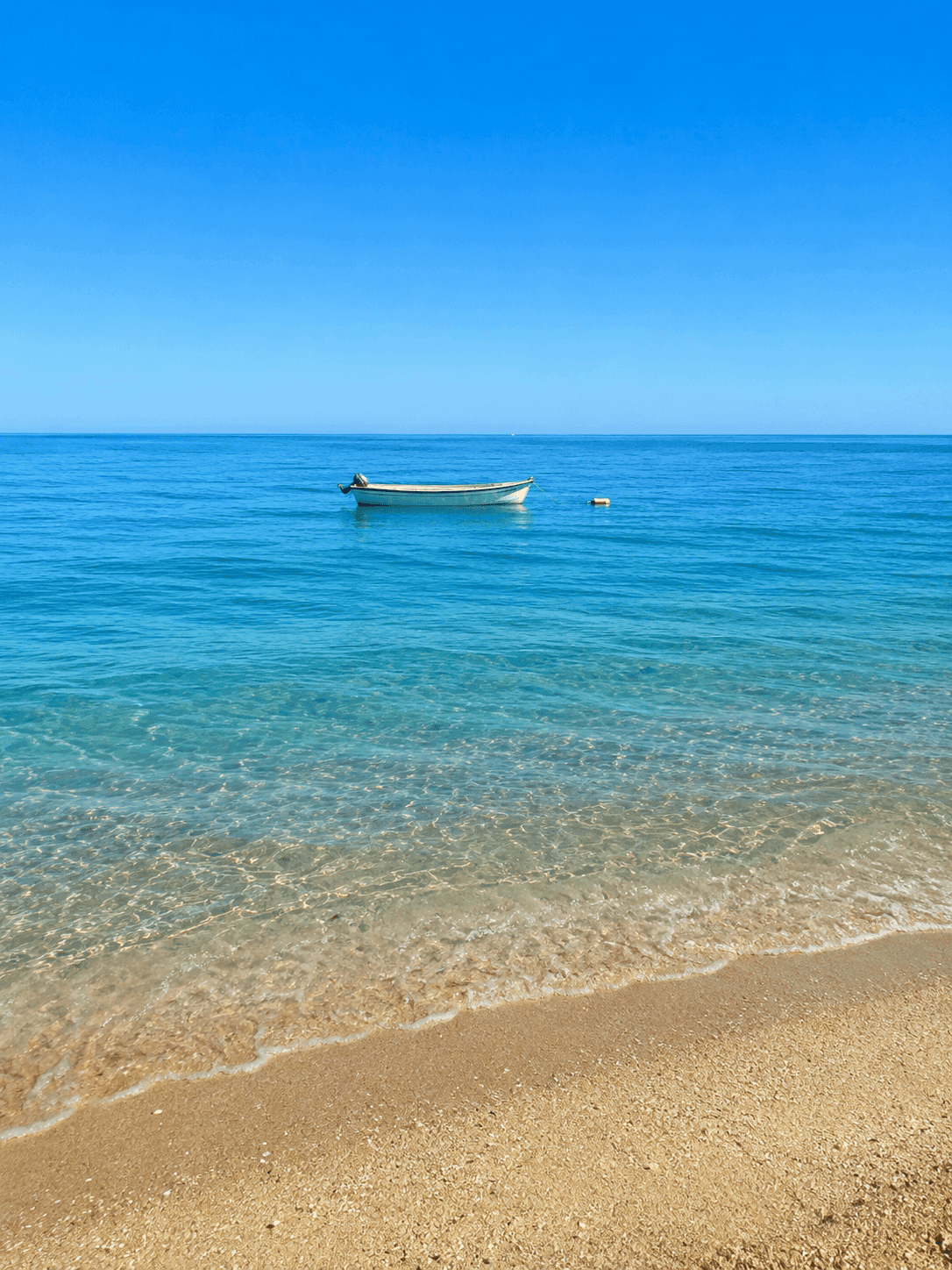 Peaceful coastal scene with a traditional boat on clear blue sea water, showcasing the idyllic natural environment near Barcelona and Maresme coastal towns.