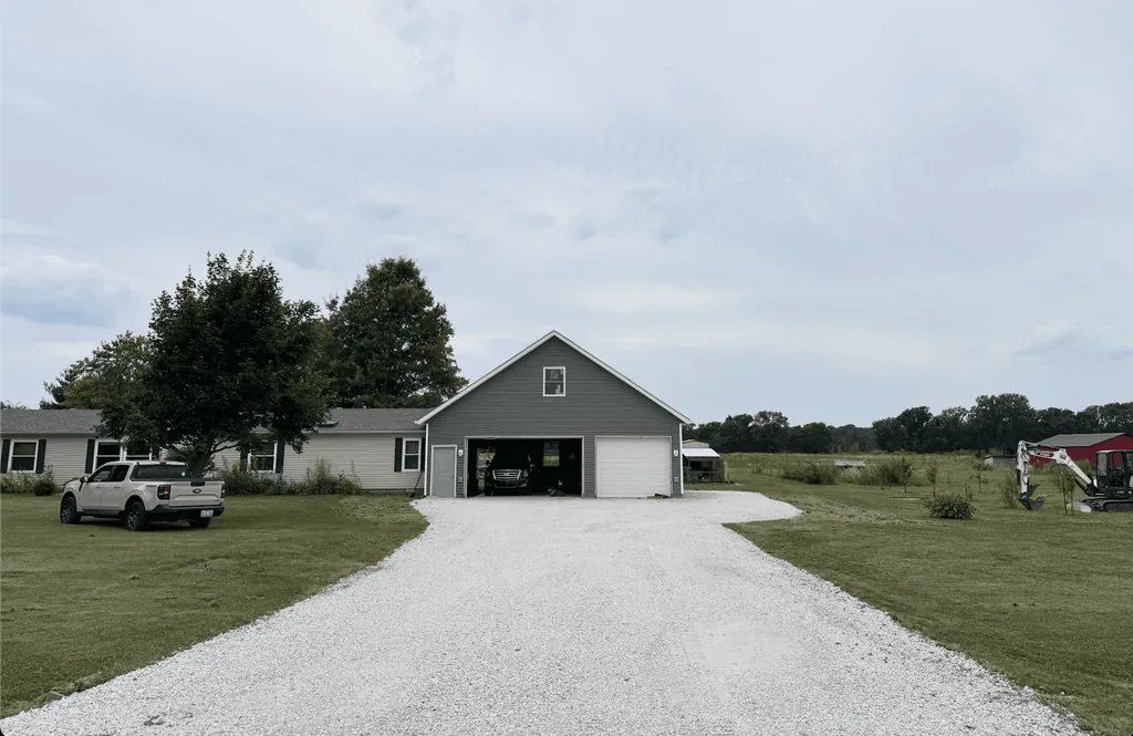 New white gravel driveway leading to a two-car garage, with a mini excavator parked at the side